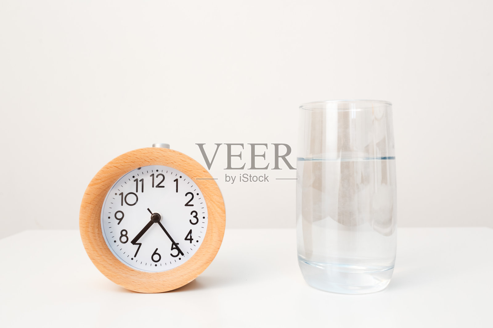 闹钟和一杯水放在白色桌子的背景上照片摄影图片