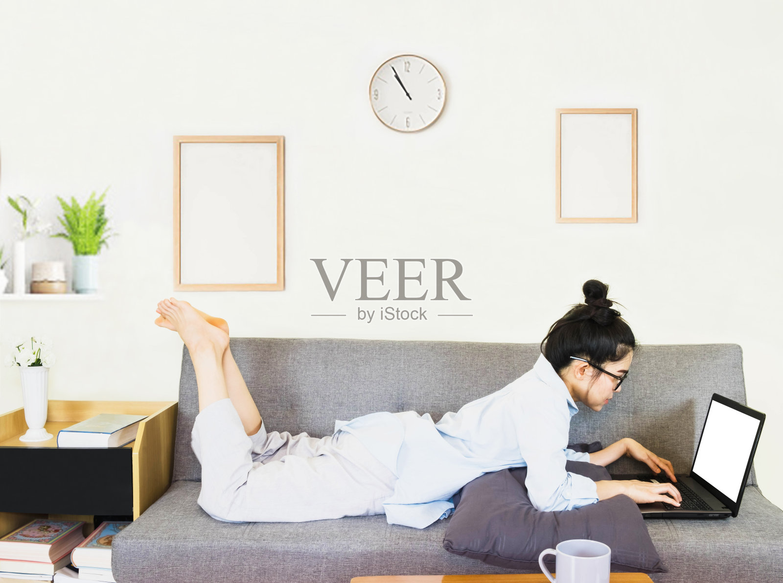 年轻美丽的亚洲女人穿着蓝色的衬衫，坐在灰色的沙发上，在线工作的生活方式，放松在家里的咖啡杯，在家工作笔记本电脑，在家工作照片摄影图片