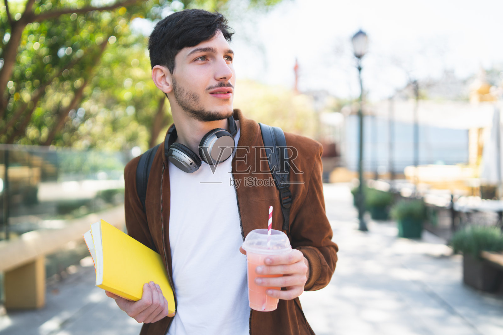 一个大学生拿着书走在街上。照片摄影图片