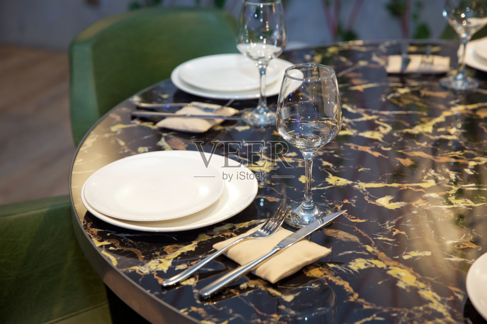 圆形大理石桌子。绿色的椅子上。一套餐具刀，匙，叉，盘，酒杯。黑色大理石桌子。照片摄影图片