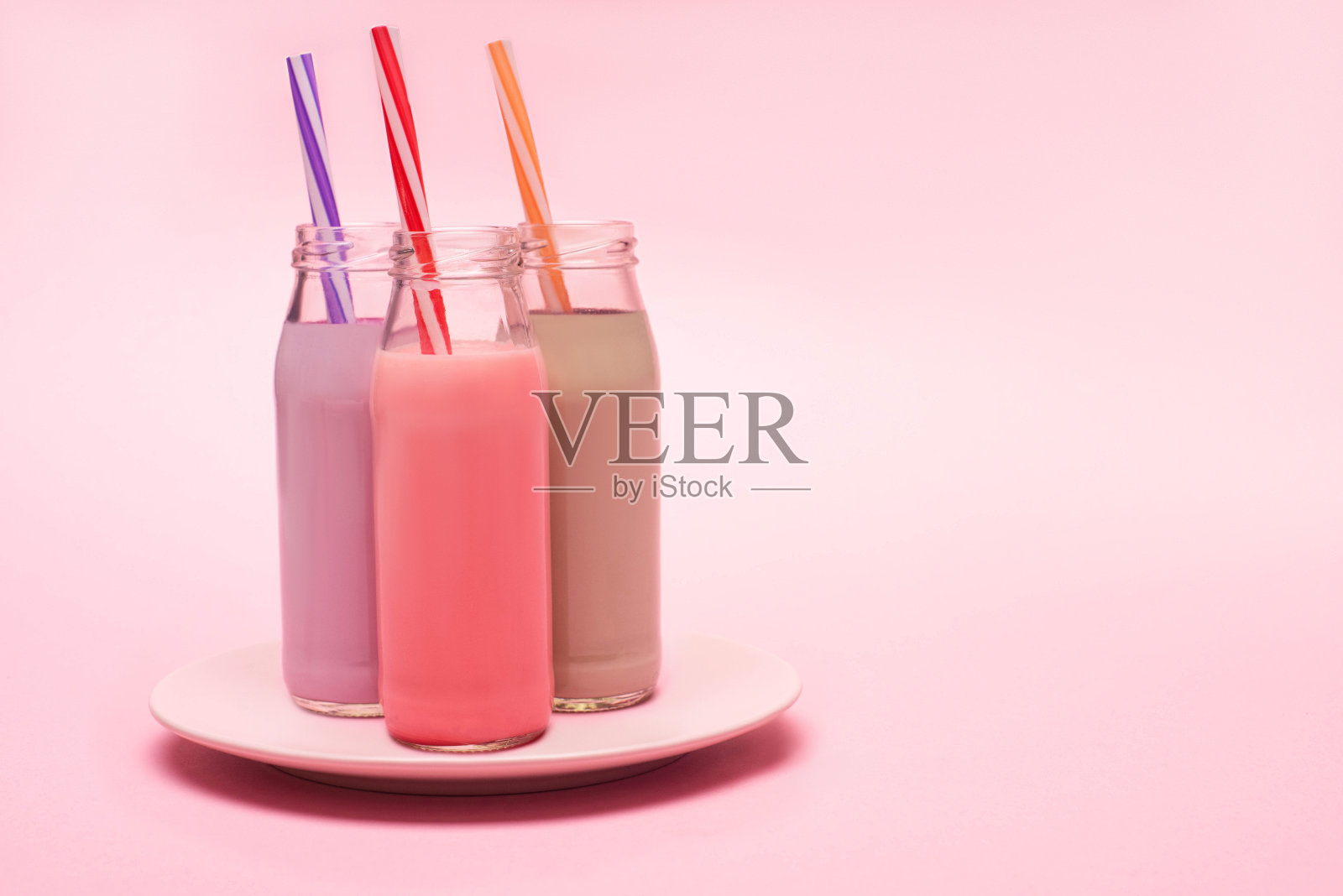 瓶子的浆果，草莓和巧克力奶昔与饮用吸管盘在粉红色的背景照片摄影图片