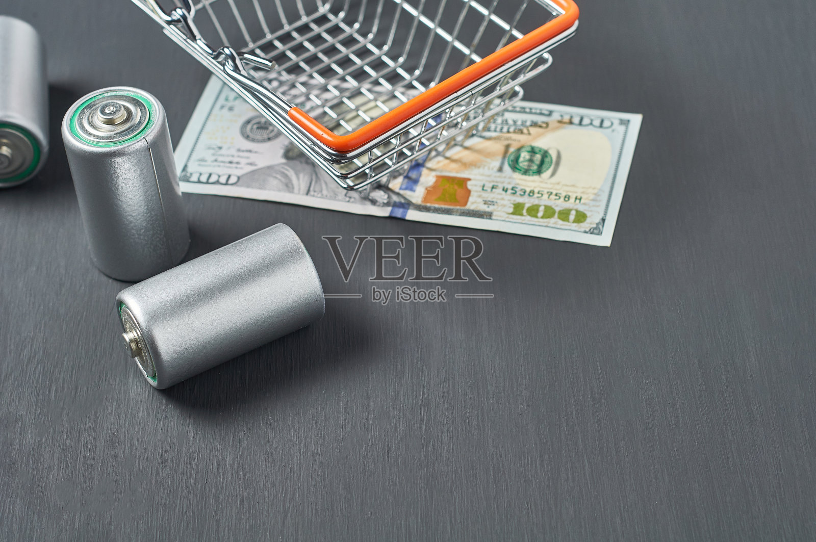 黑色的水泥桌子上的金属篮子里放着旧电池和百元钞票。回收的概念。拯救环境。电费、购销费用照片摄影图片