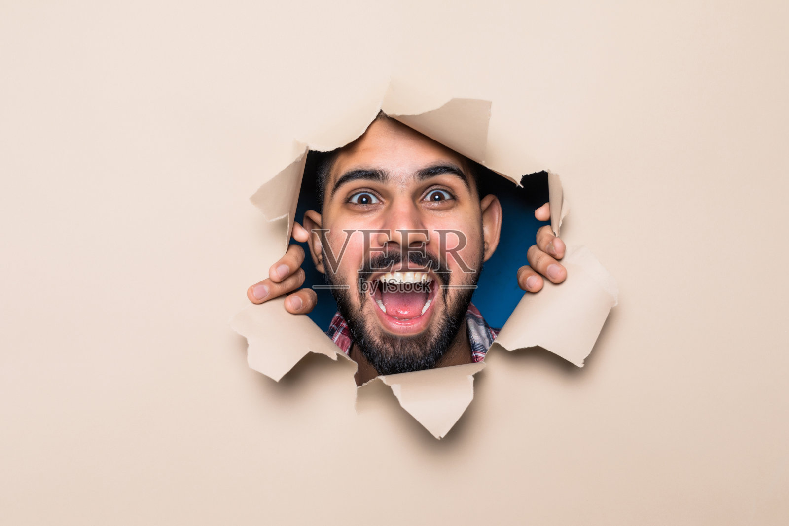 年轻英俊的男子透过米黄色的纸洞看照片摄影图片