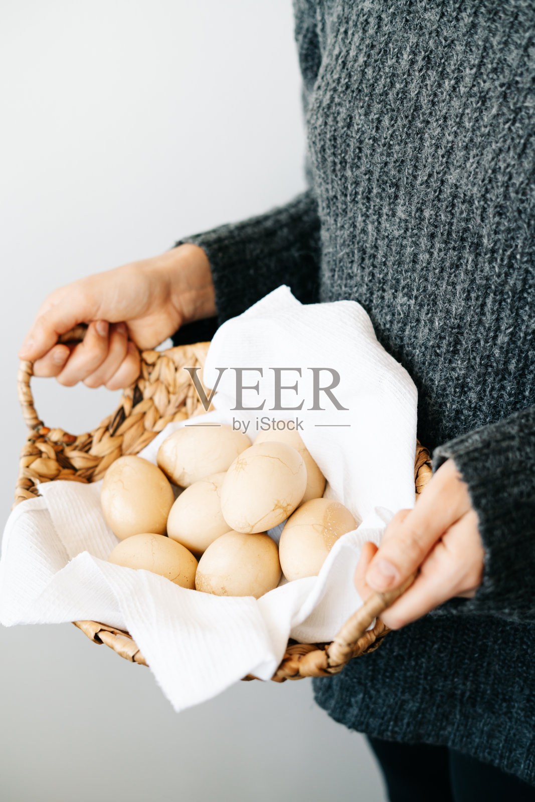 一个女孩穿着一件灰色针织羊毛衫，拿着一个天然柳条篮子，篮子里放着用时髦的蜡笔画的复活节彩蛋，蛋壳上还有裂缝。最小的风格。为文本复制空间。复活节的概念照片摄影图片