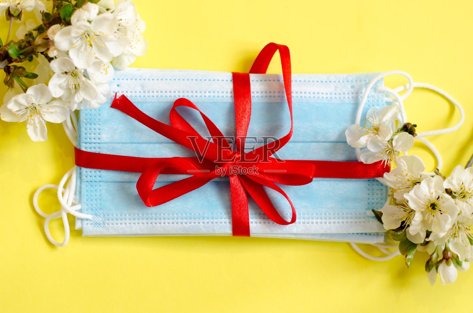 黄色背景带花的医用口罩。冠状病毒保护。对抗病毒的天赋。花的背景。照片摄影图片