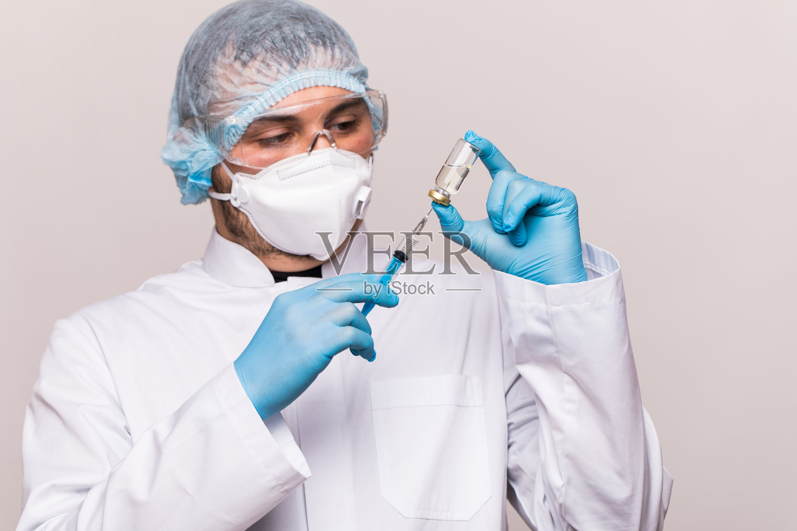 COVID-19感染。男医生检查药物为疾病，男子在蓝色面具与注射器和罐子照片摄影图片