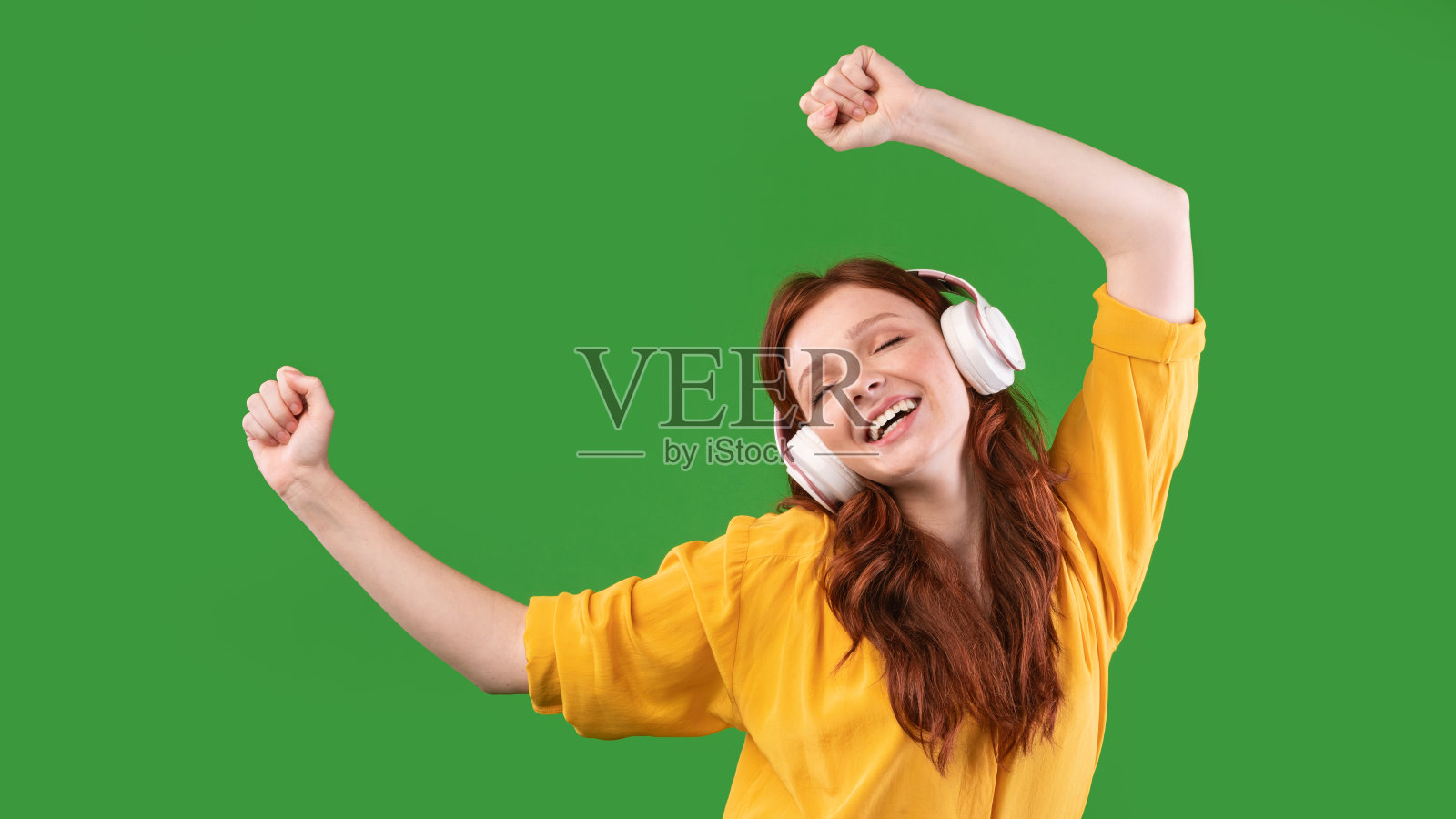 快乐的女孩戴着耳机在绿色背景下跳舞，全景图照片摄影图片