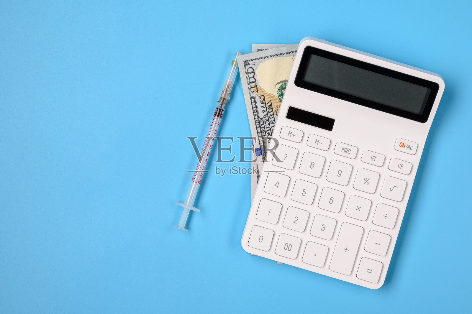 一个医生的工作场所，有一个计算器，钱和一个注射器在一个蓝色的背景空白文字。照片摄影图片