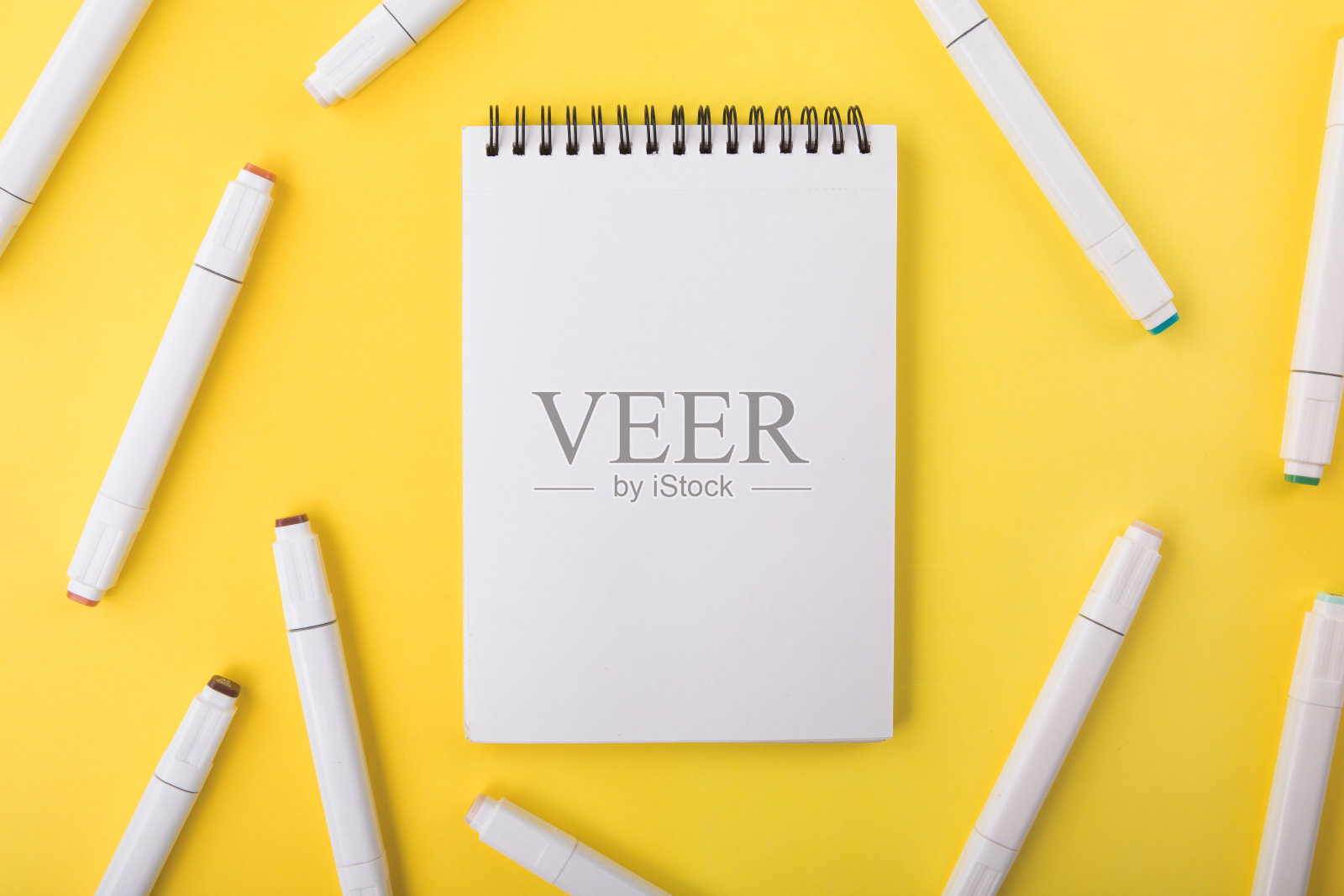 不同颜色的标记，黄色背景上的白色记事本，俯视图。照片摄影图片