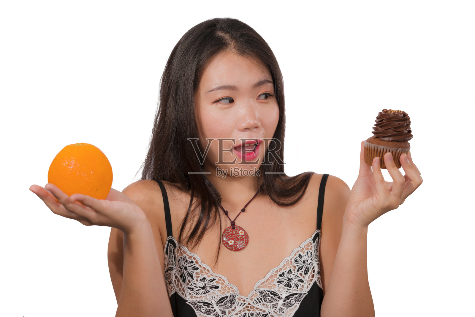 年轻有魅力和快乐的亚洲韩国女人拿着美味和诱人的巧克力纸杯蛋糕充满卡路里和新鲜健康的橙子低卡路里，而不是含糖的垃圾食品照片摄影图片