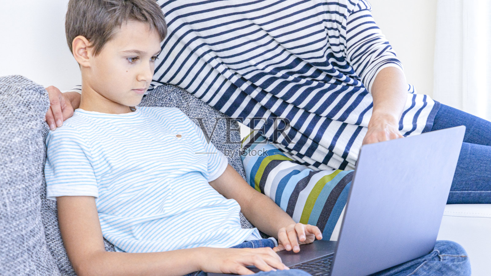 孩子在家里用笔记本电脑在线学习。妈妈帮他，解释任务。技术，在线学习，远程教育，在家学习，家庭作业，在家工作照片摄影图片