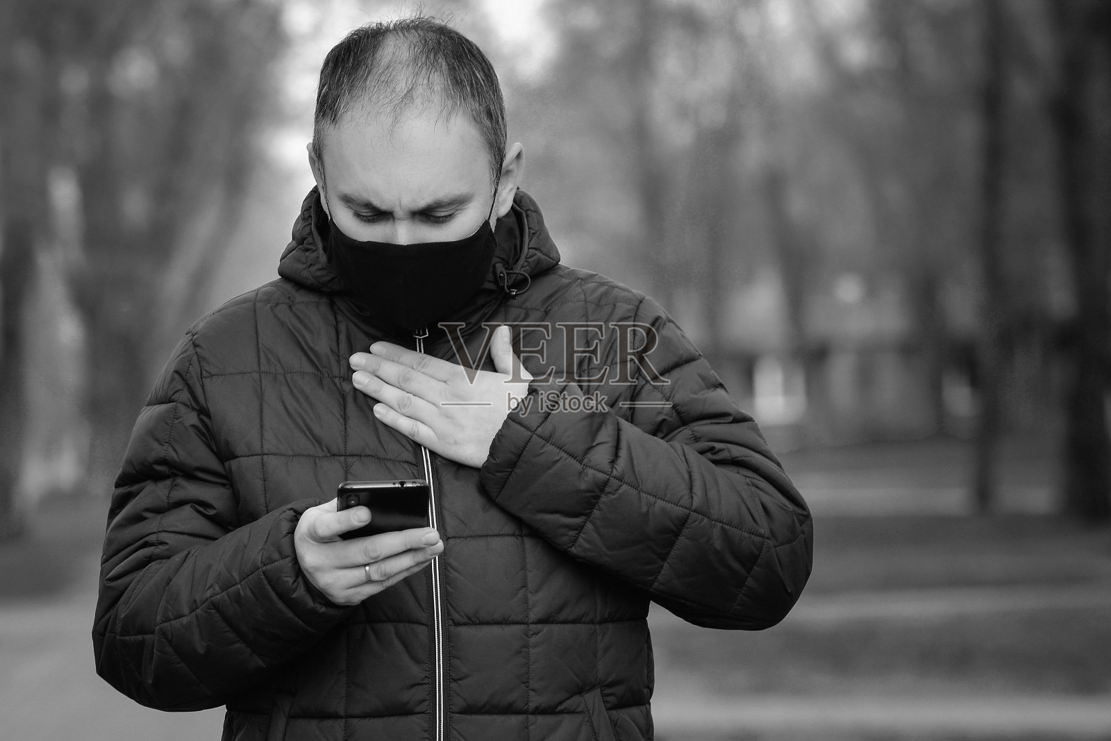 忧心忡忡的男性戴着黑色防护面具，在户外用智能手机查看新冠病毒的最新消息照片摄影图片