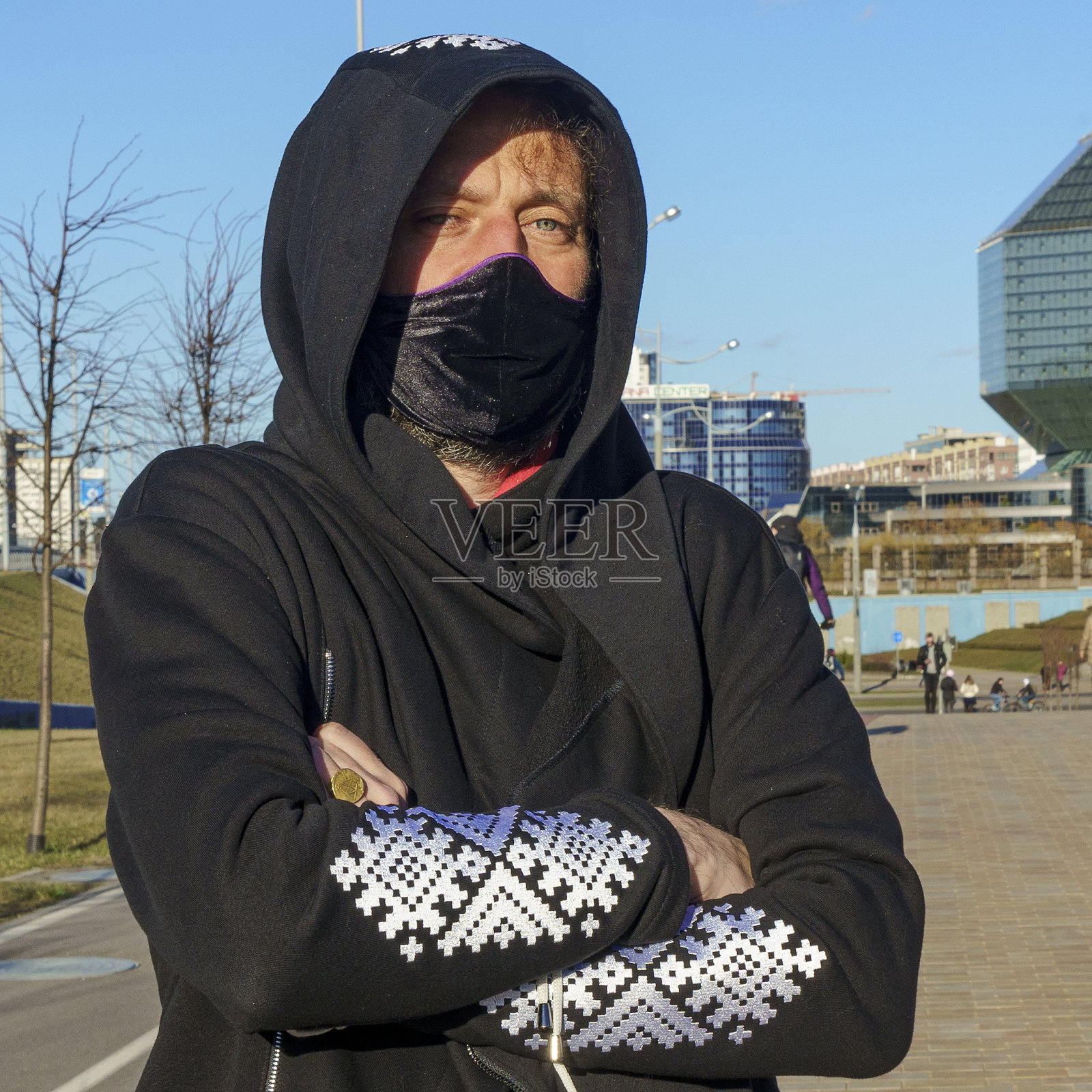 这名男子戴着医用防护面具，穿着印有斯拉夫装饰的运动衫，背景是经典的蓝天。Covid-19概念。空间的文本。照片摄影图片