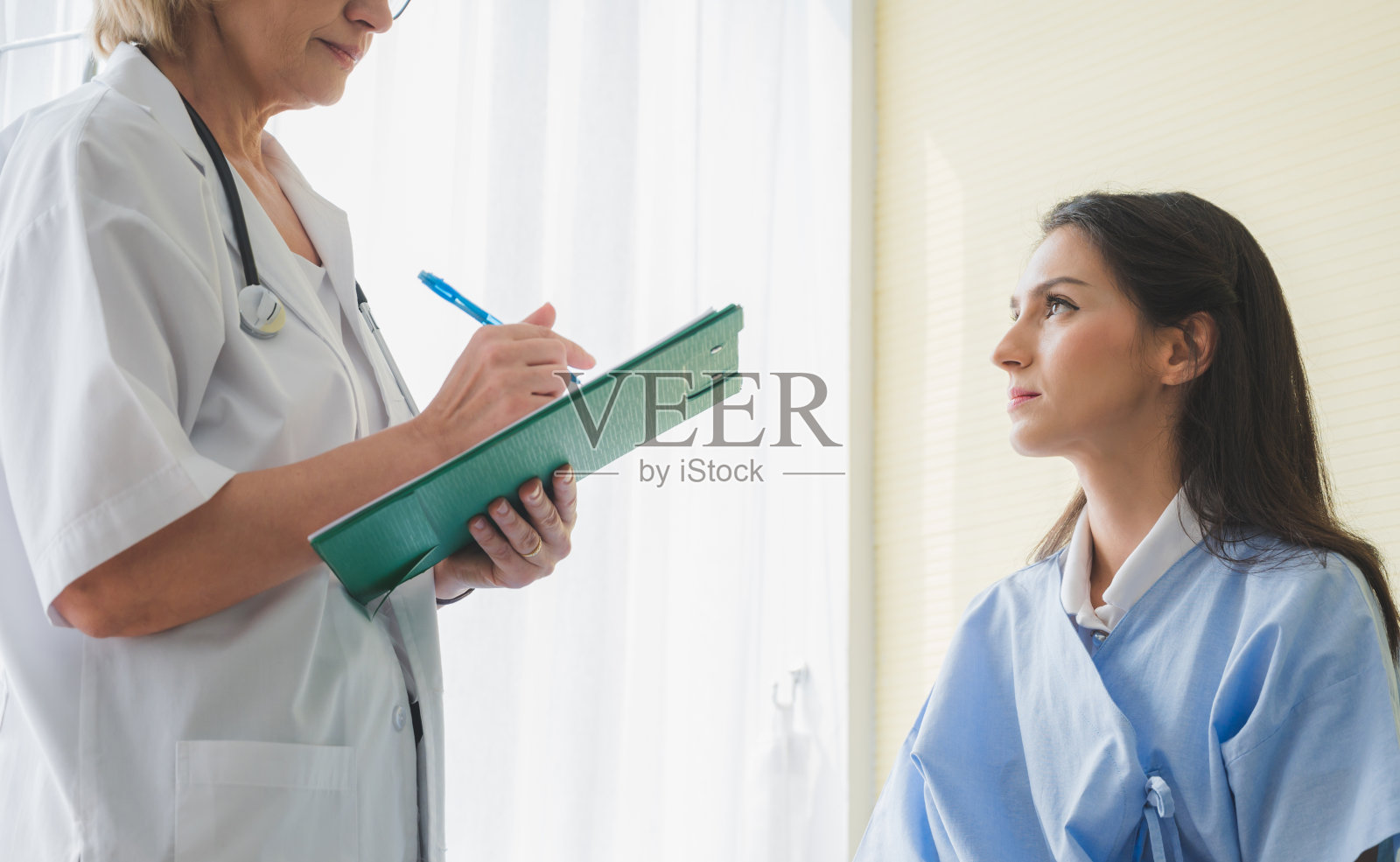 资深女医生和病人坐在床上讨论并记录症状问题。照片摄影图片