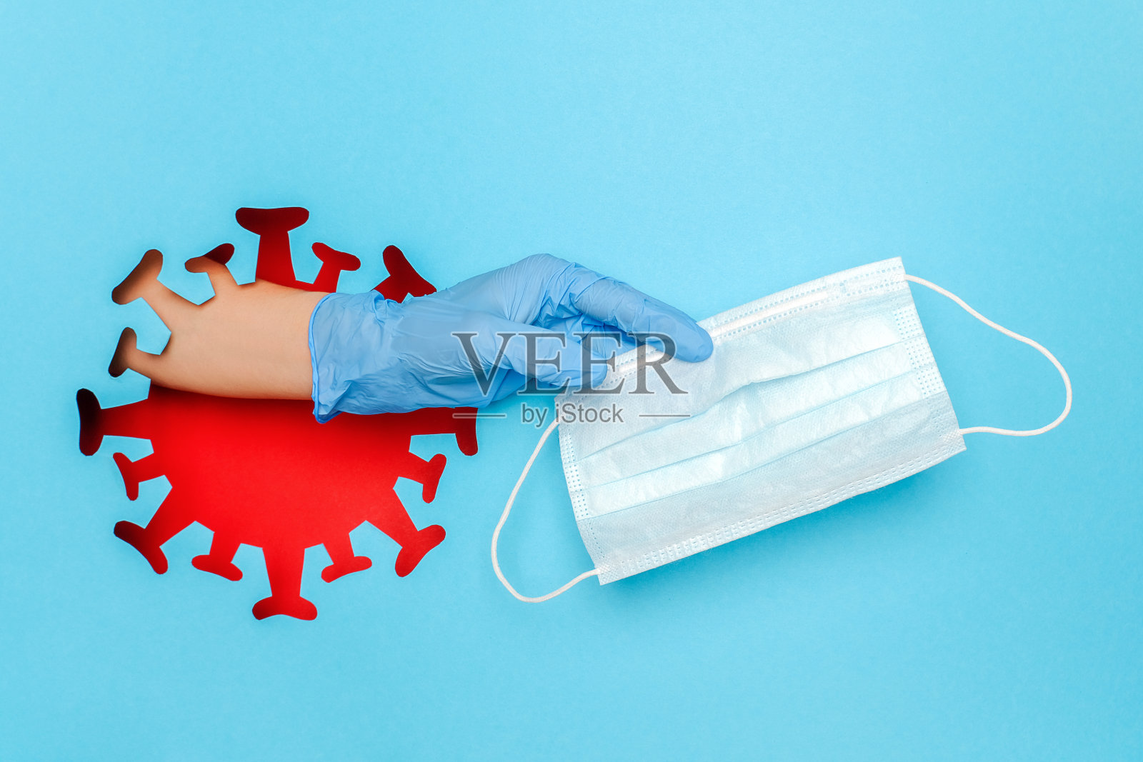 在蓝色背景上，以红色冠状病毒、病毒、细菌、微生物为形式，手持乳胶手套，从小孔中穿出医用口罩。创新防控新冠肺炎和传染病理念照片摄影图片
