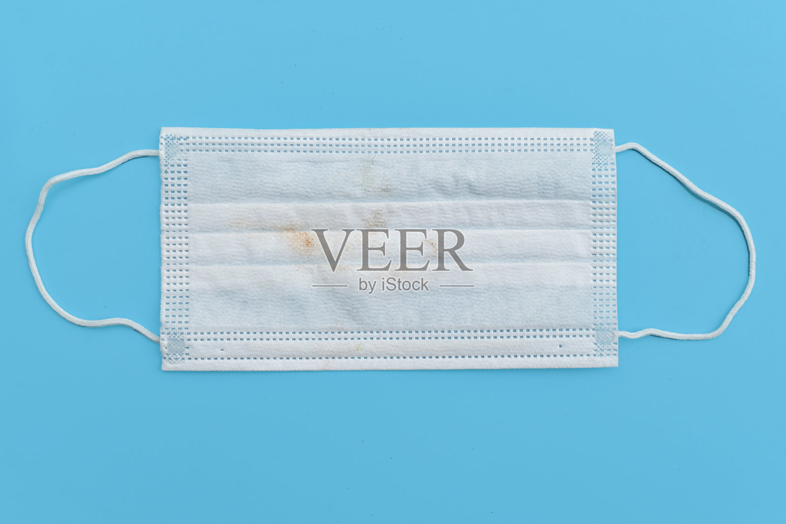 使用过的医用口罩，在蓝色背景上使用后会更脏和污染。一次性外科口罩盖住口鼻。保护健康和医疗理念照片摄影图片