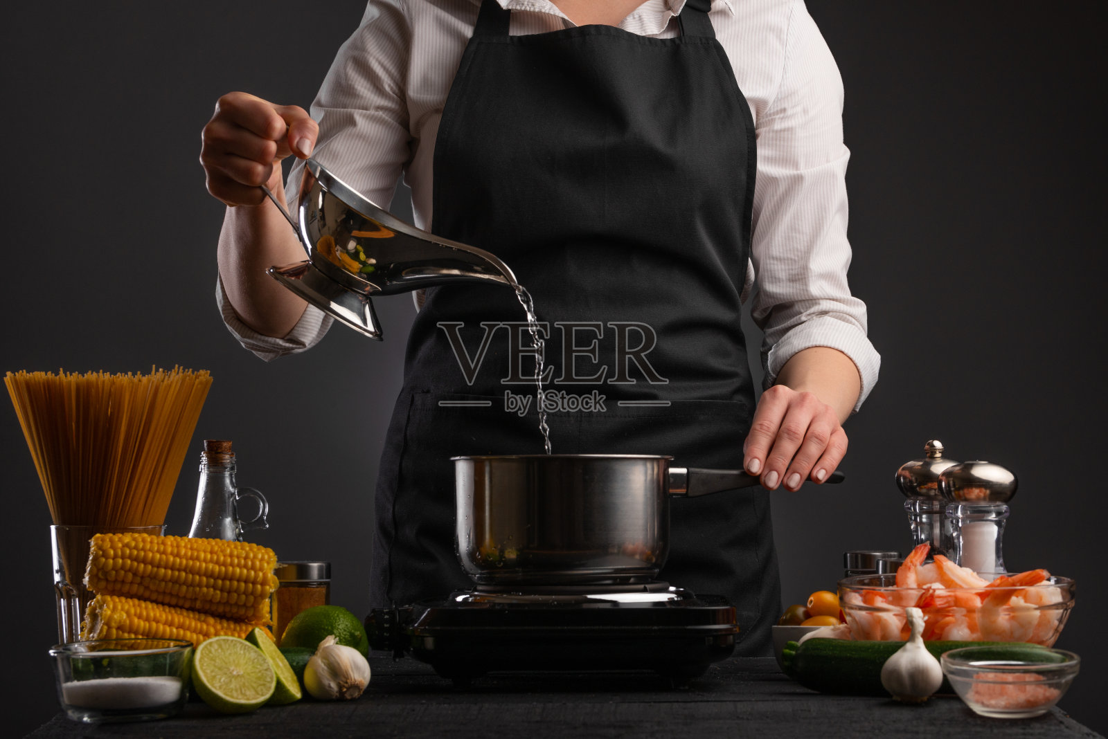 厨师将水倒入平底锅煮意大利面。冻结。背景材料为烹饪，虾和蔬菜照片摄影图片