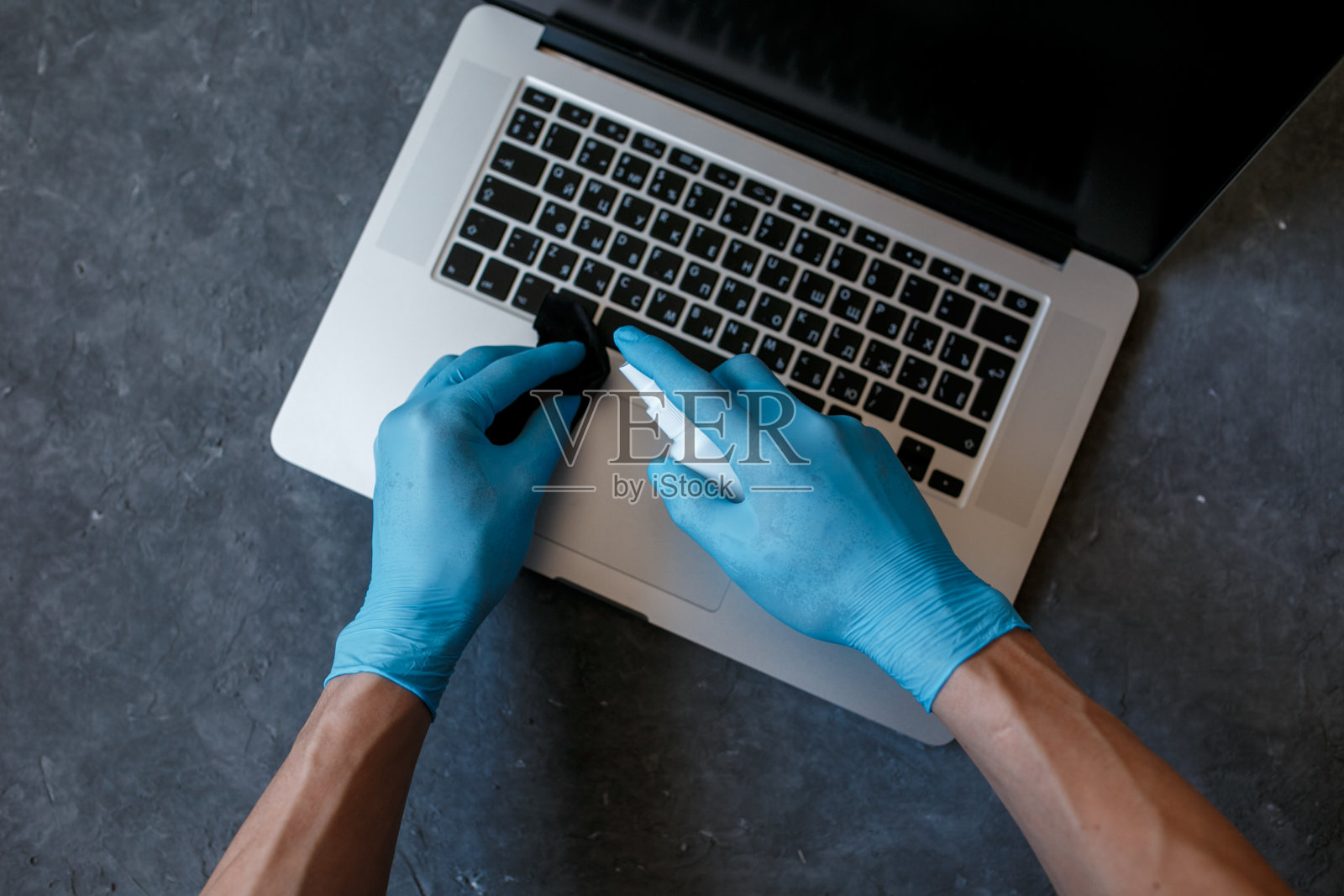 对计算机进行covid-19病毒消毒。在你的电脑上喷洒防冠状病毒的消毒剂。在家的概念工作照片摄影图片