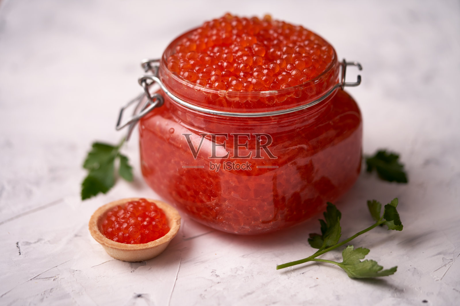 红色的鱼子酱，到一个装满鱼子酱装饰勺子的玻璃罐的顶部，一个鱼子酱馅饼，绿色躺在白色的石头纹理背景。海鲜,三文鱼鱼子酱照片摄影图片