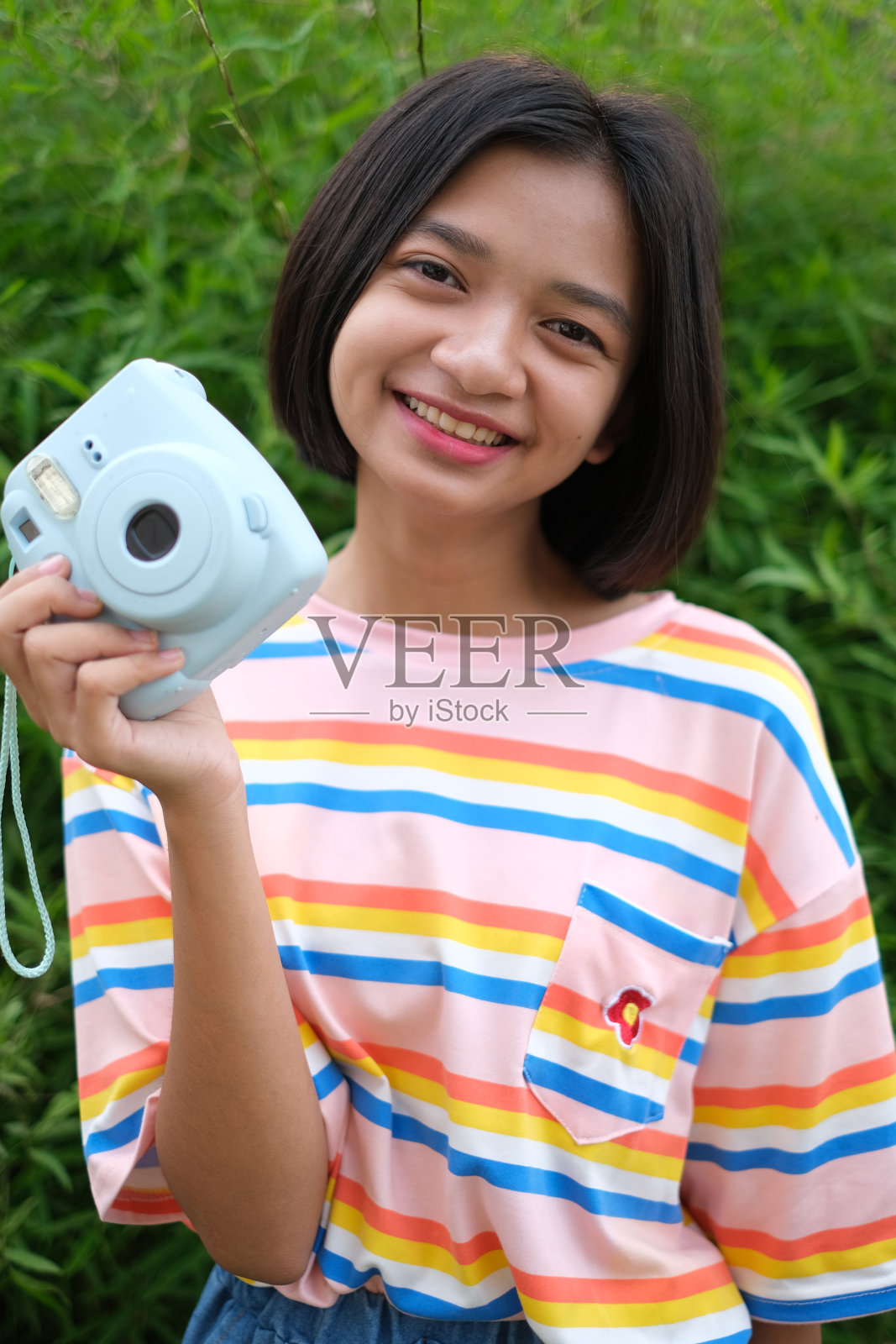 快乐的年轻亚洲女孩与蓝色相机和自然背景。照片摄影图片