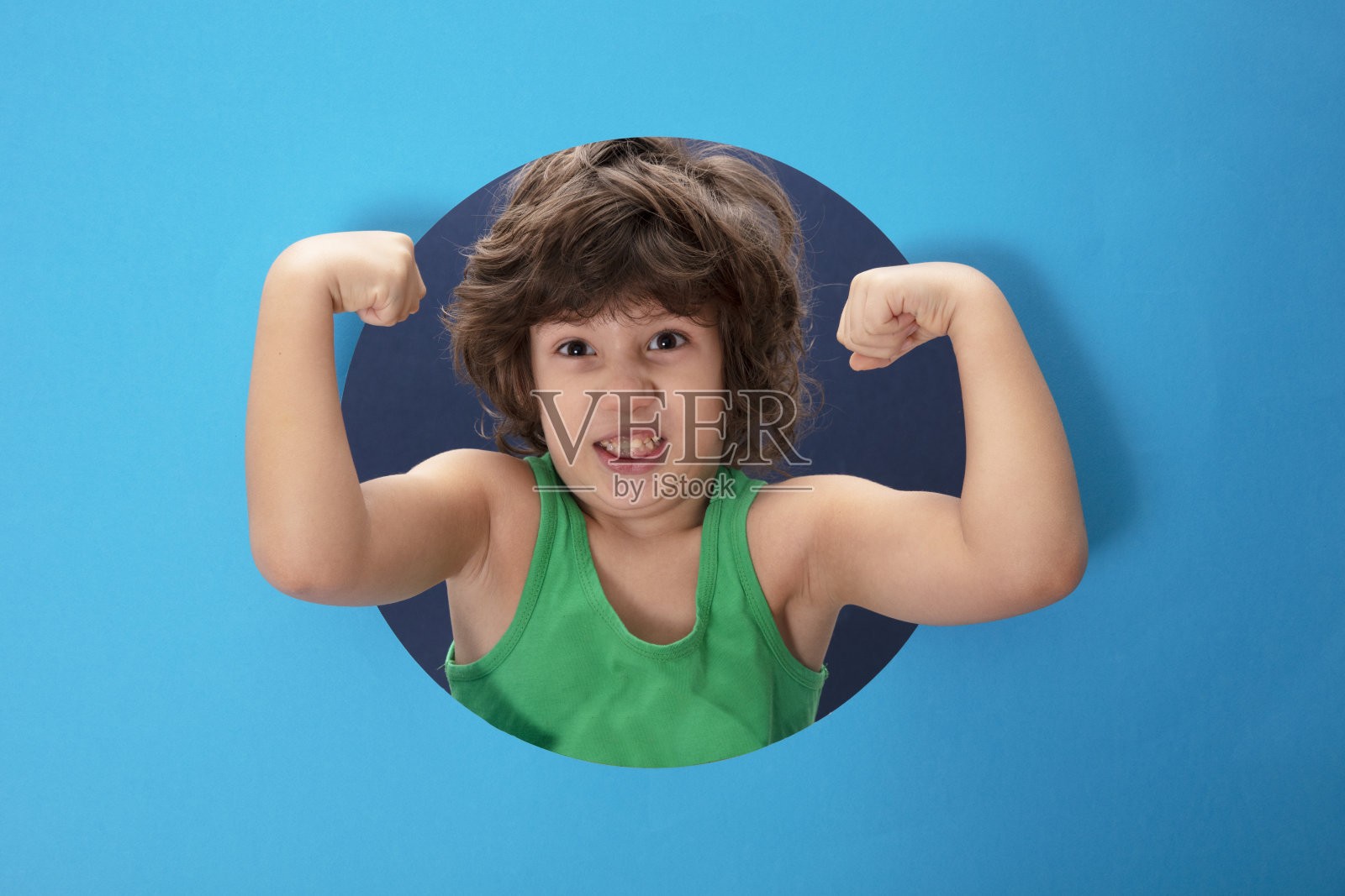 强壮的孩子穿着一件绿色的t恤，双手穿过撕破的纸洞。照片摄影图片