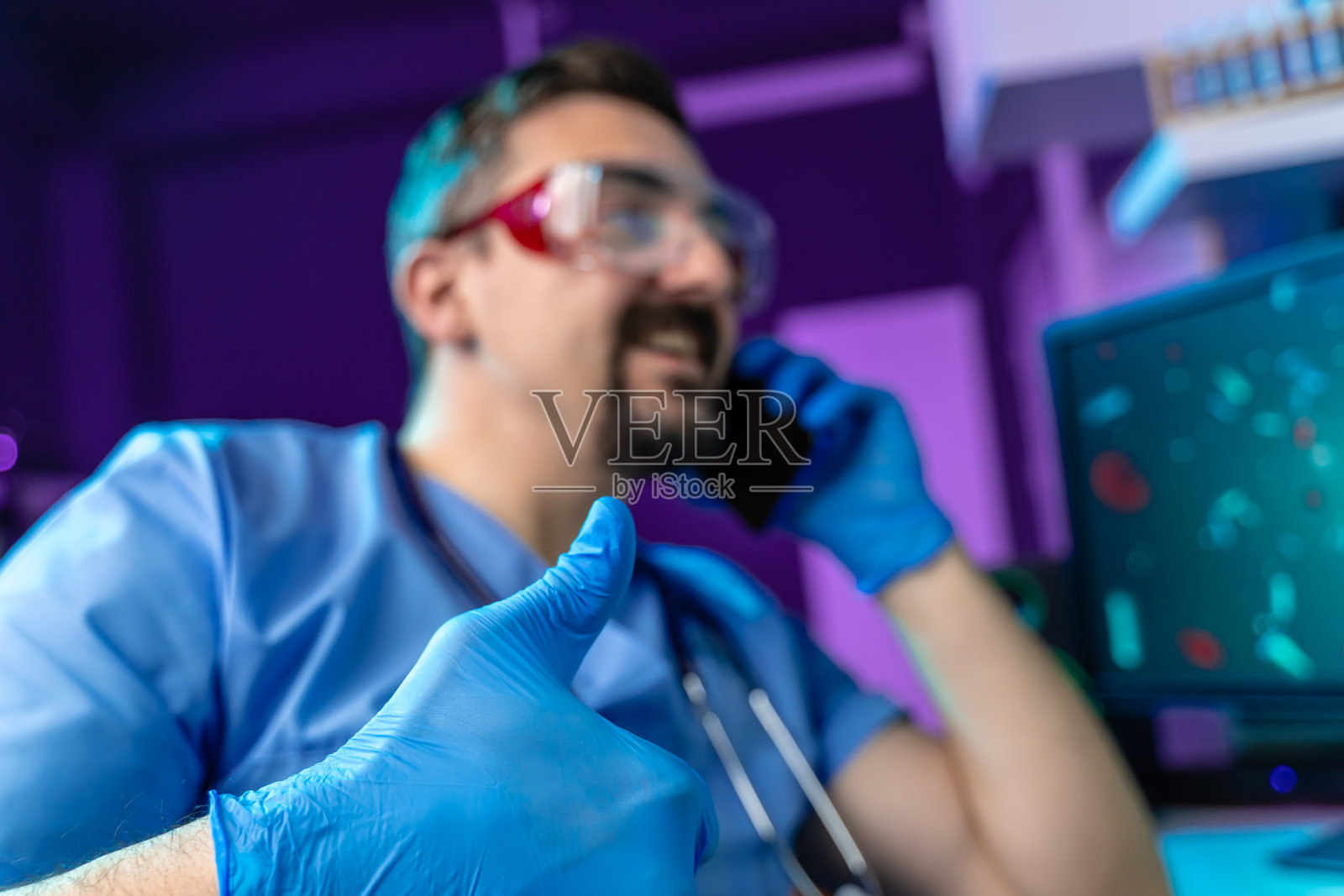 医生戴着防护眼镜，微笑着用手机交谈，竖起大拇指照片摄影图片