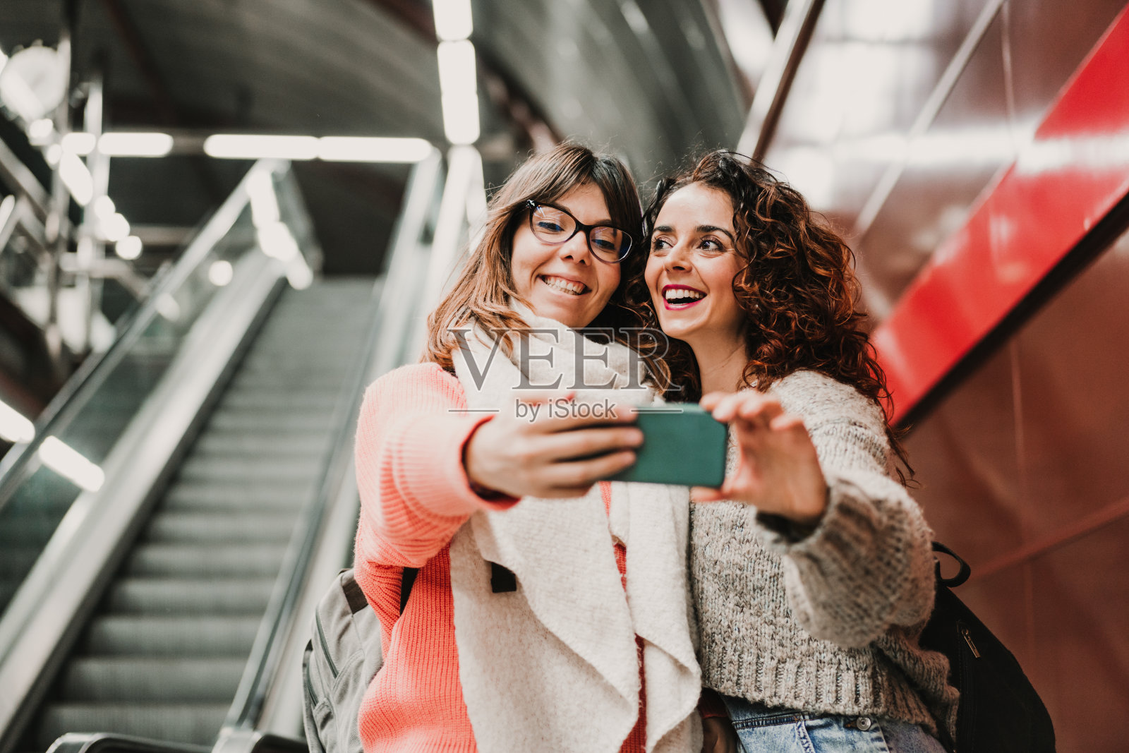 两个朋友在车站等着下楼梯，等着赶火车。用手机自拍。旅游摄影。的生活方式。照片摄影图片