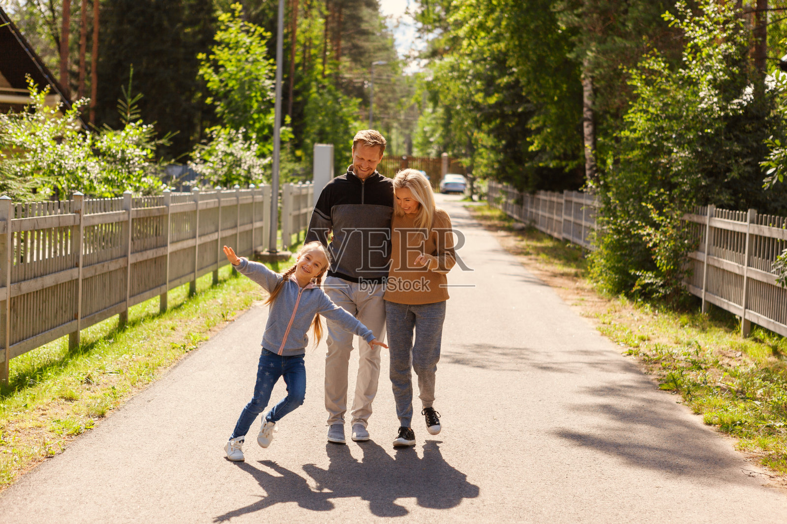 快乐的家庭在乡下度过周末。这对夫妇微笑着走在路上，拥抱着，看着他们顽皮的小女孩跑来跑去，看着镜头照片摄影图片
