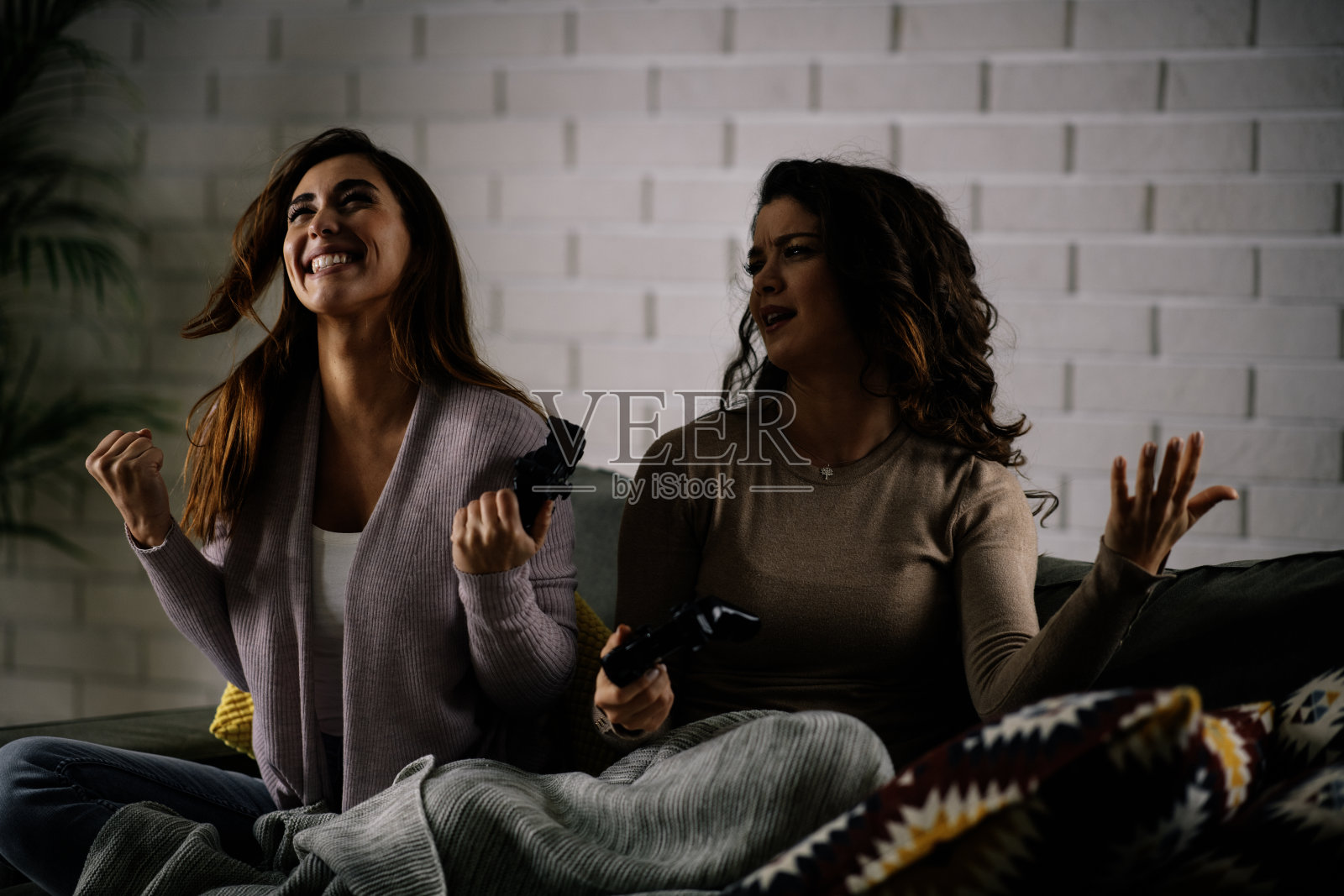 漂亮的女朋友坐在沙发上玩电子游戏。照片摄影图片