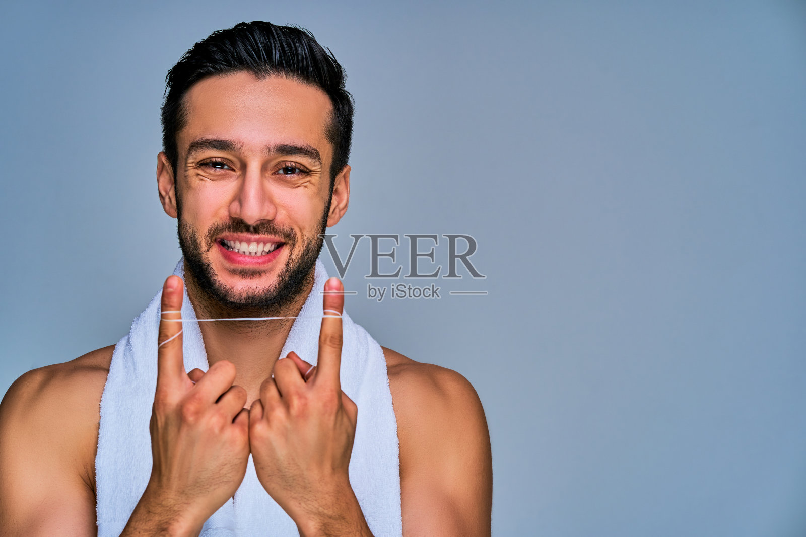 特写的家伙与宽微笑的黑发和胡子显示了手上的牙线。牙科的概念照片摄影图片