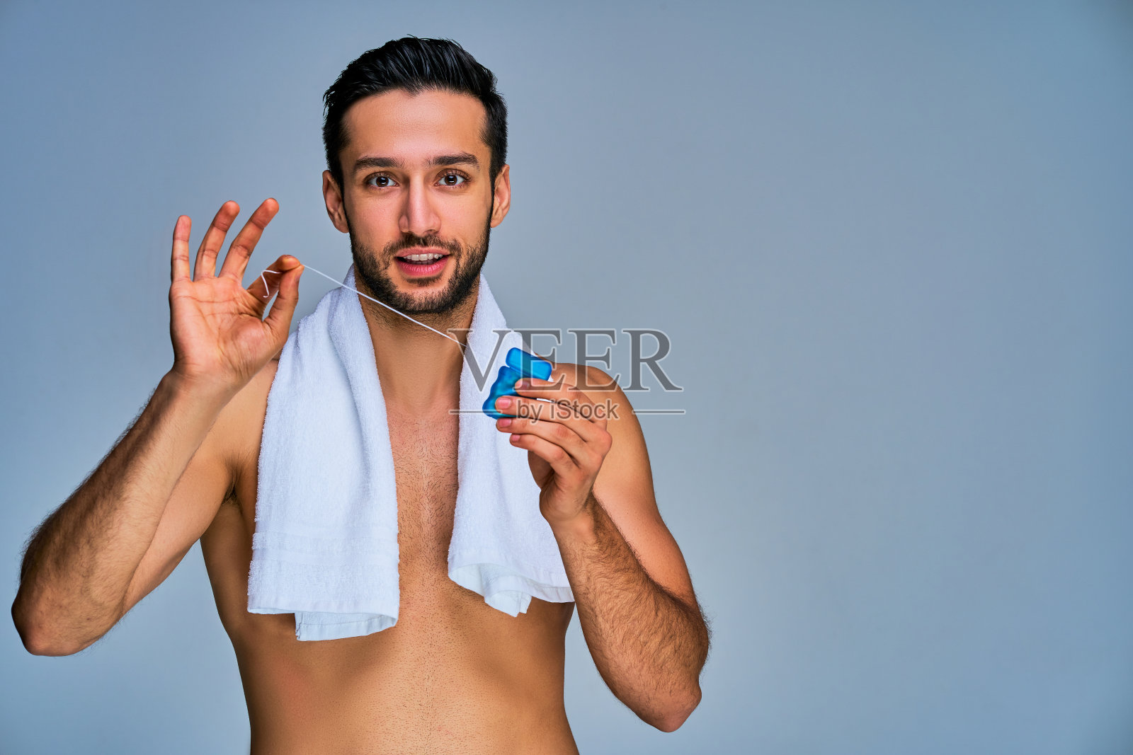 一个黑头发、留着胡子、面带微笑的家伙，手上拿着一盒蓝色的牙线。牙科的概念照片摄影图片