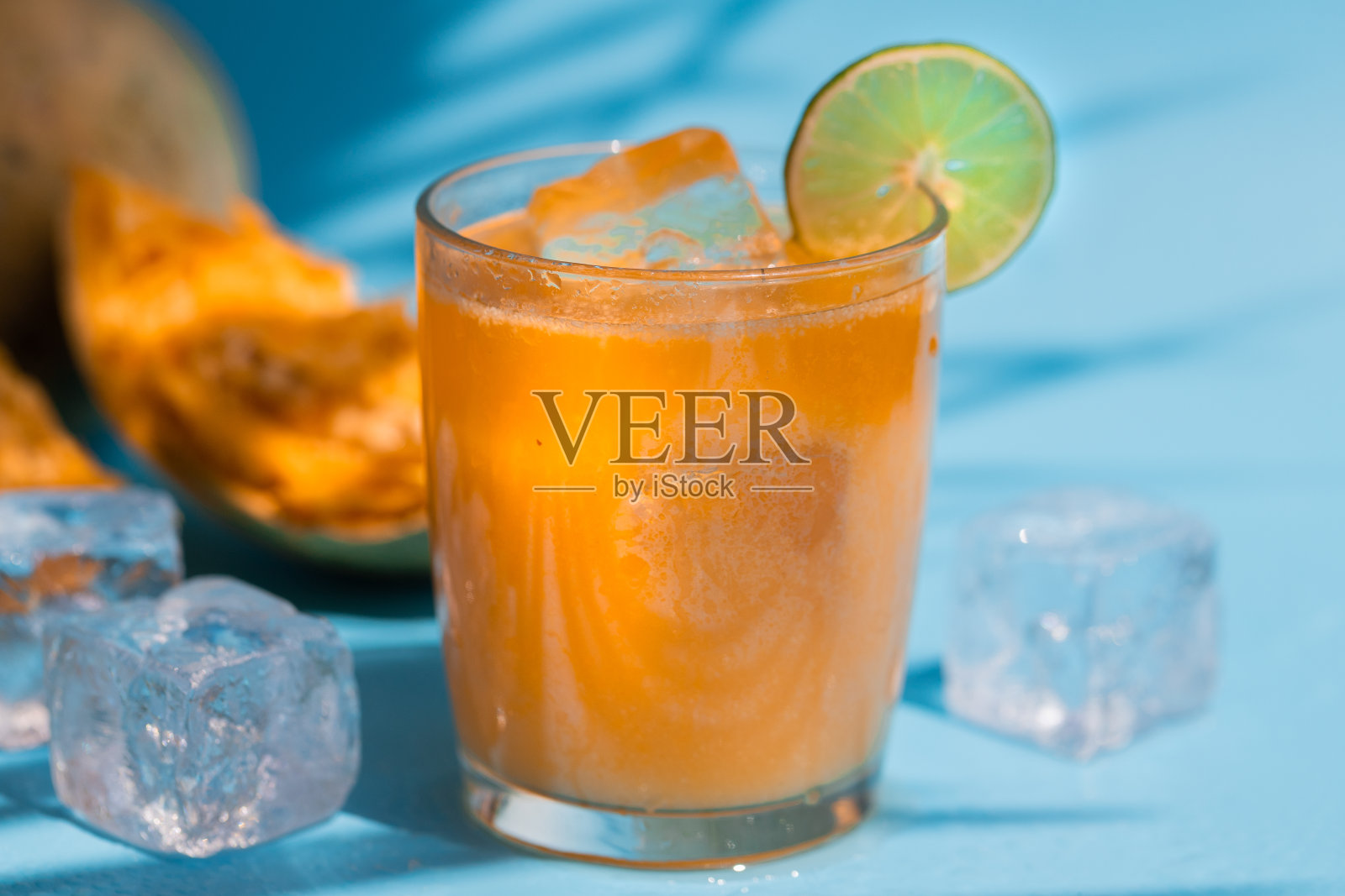 来自Bel fruit或木苹果的异国果汁，在印度被称为Bel Ka Sharbat。冷水果饮料与冰在蓝色背景明亮的阳光与棕榈叶的阴影照片摄影图片