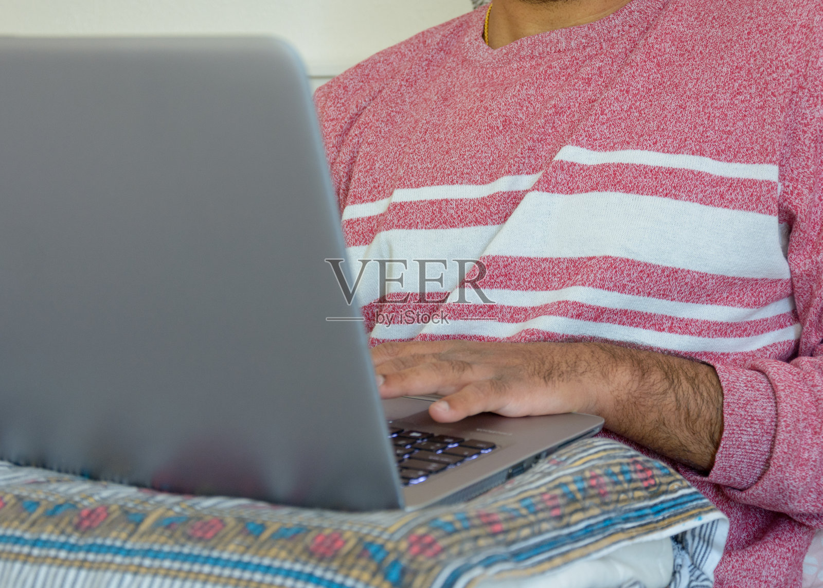 新冠肺炎大流行期间，一名成年男性在卧室用枕头支撑笔记本电脑工作的临时工作区照片摄影图片