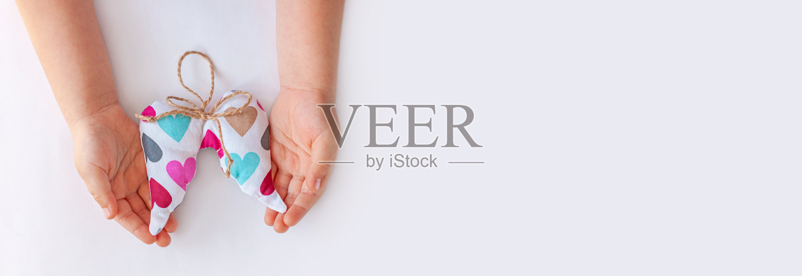 孩子们的手握着柔软的天使翅膀，用五颜六色的心和黄麻线把弓平躺着。捐赠的概念,周二照片摄影图片