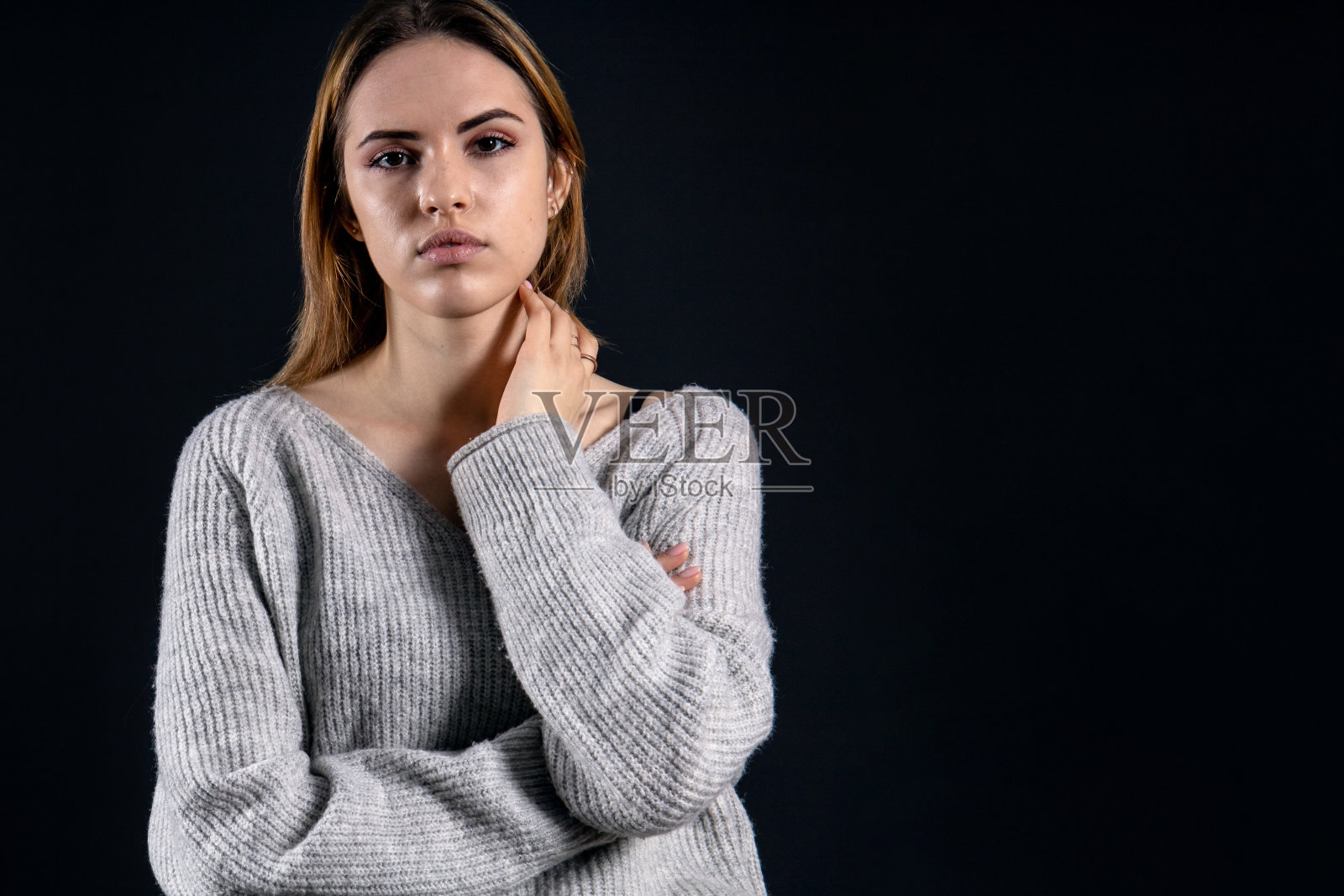 年轻美丽的女孩在灰色毛衣与一个平静沉思的表情在一个黑暗的背景，复制空间照片摄影图片