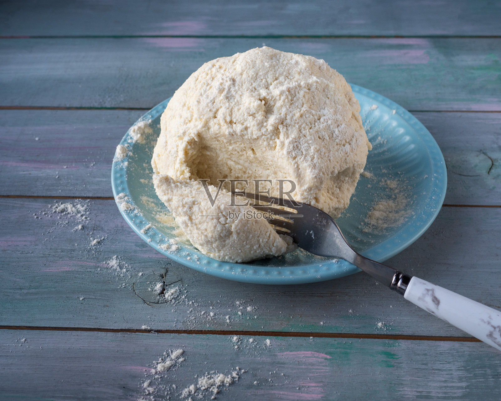 懒人饺子用的凝乳面团放在陶瓷蓝盘子里，木桌上放一汤匙照片摄影图片