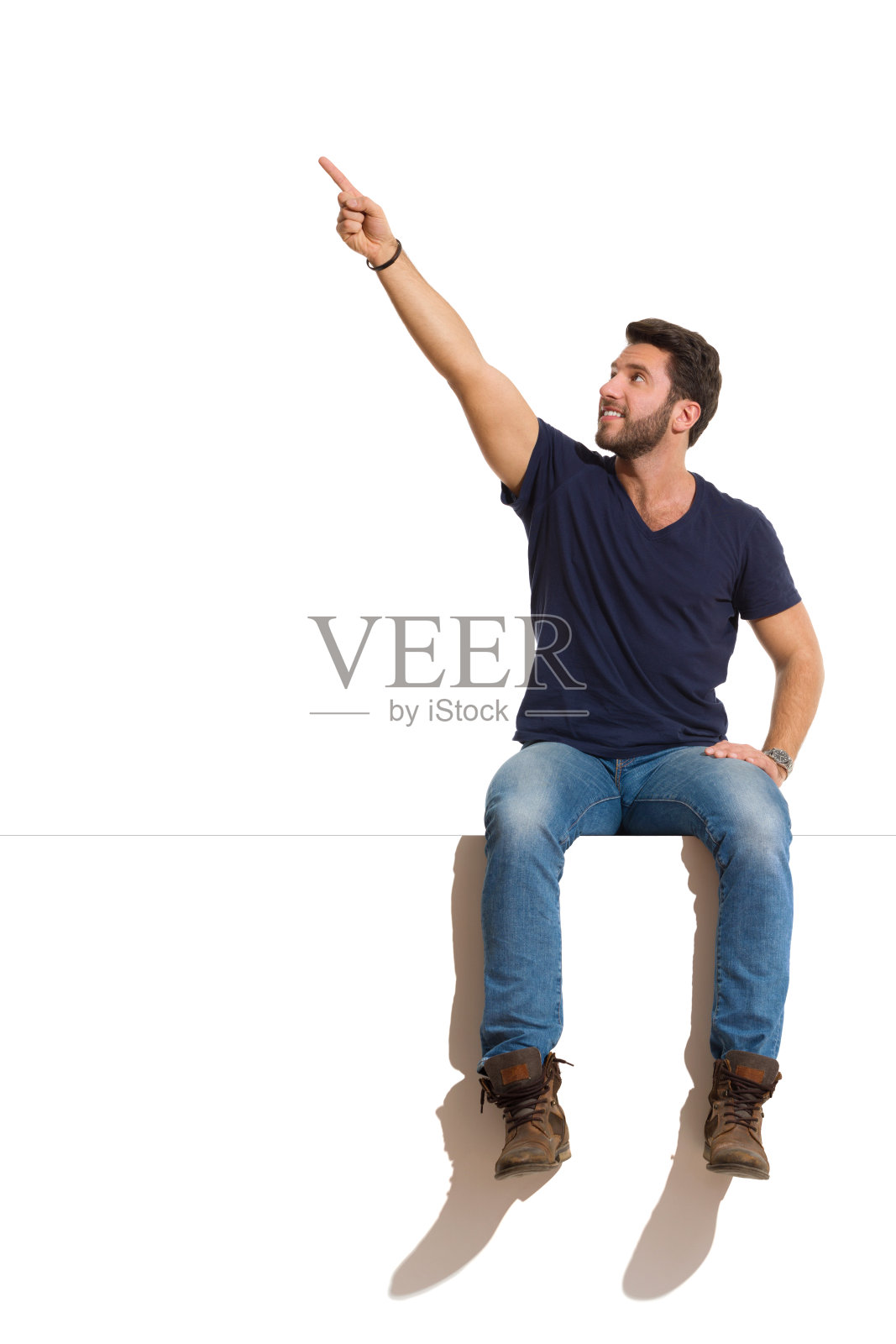 英俊自信的男人坐在顶端，看向远方并向上指照片摄影图片