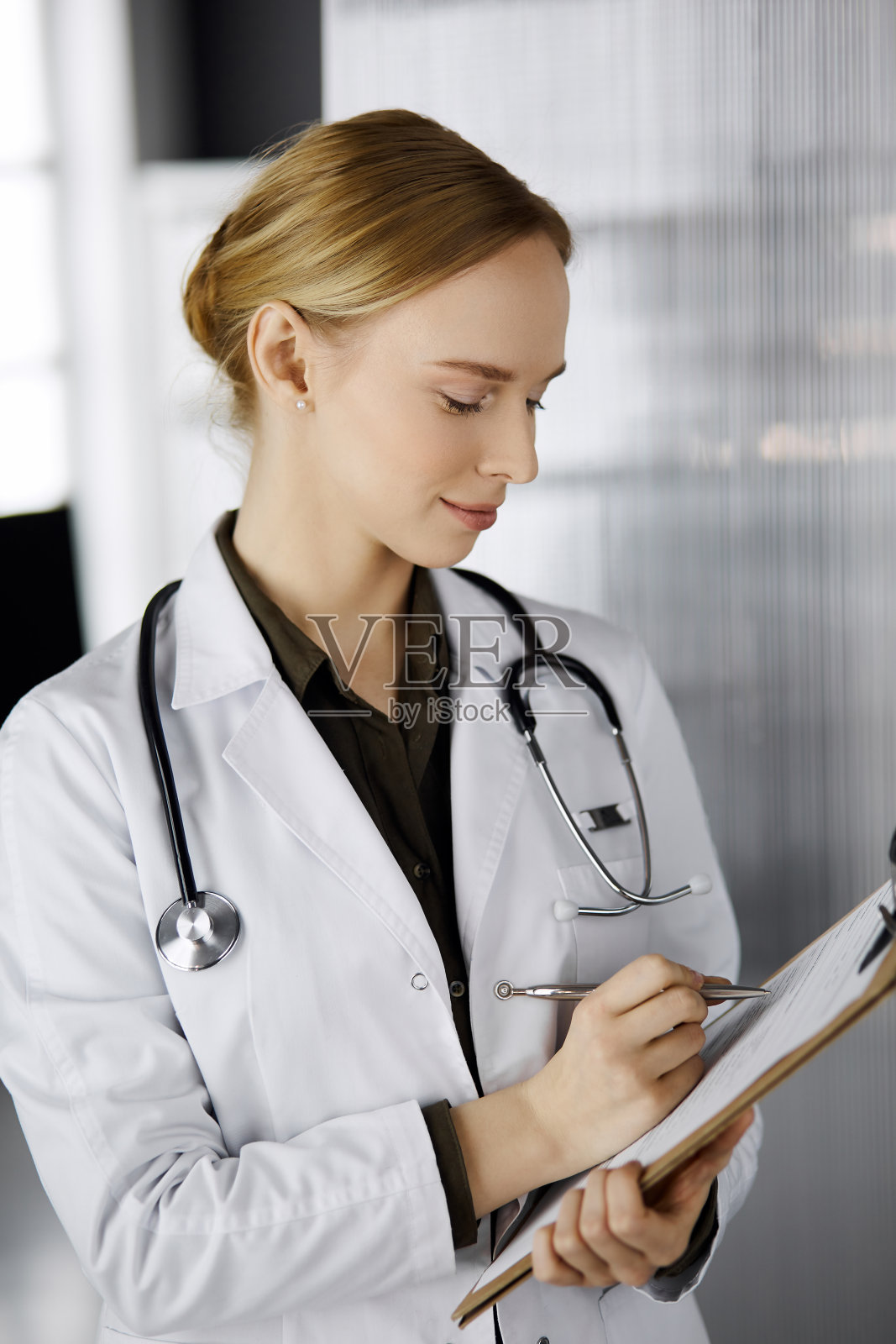 笑容开朗的女医生在诊所使用剪贴板。友善的女医生在工作的肖像。医院完善的医疗服务。医学的概念照片摄影图片