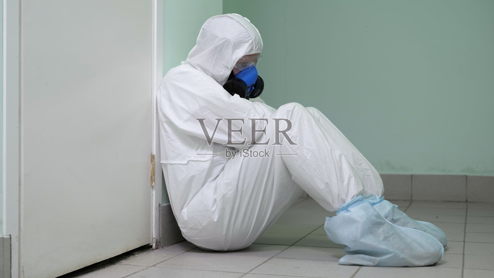 疲惫的医生穿着危险服坐在地板上睡觉。O照片摄影图片