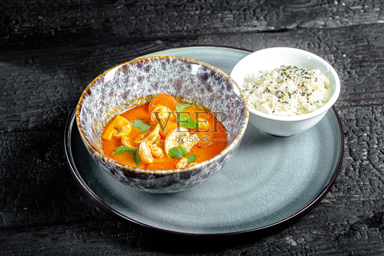 背景黑色烧焦的木头，结构，深蓝色的盘子，泰国冬阴汤，米饭在碗里照片摄影图片