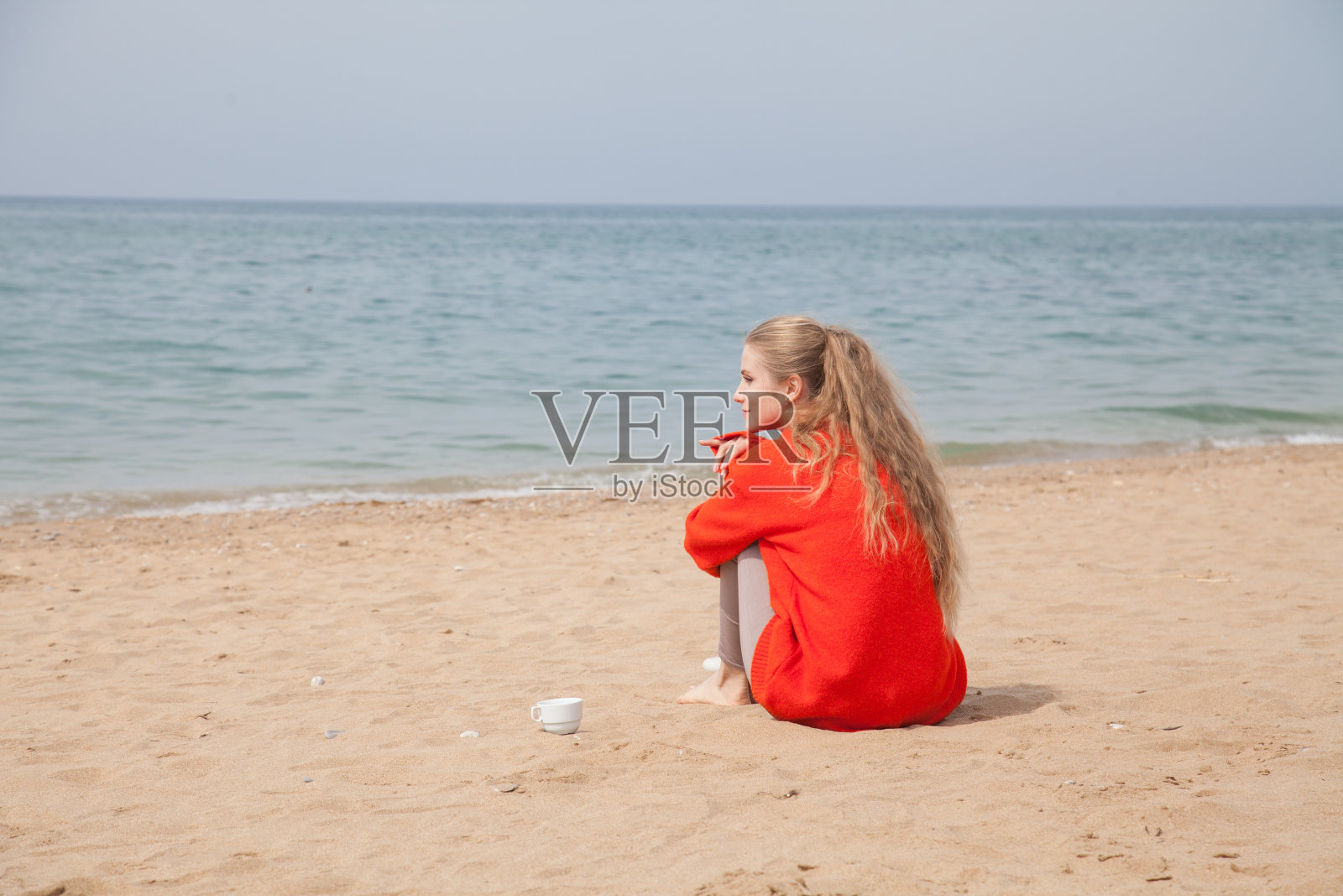 一个美丽的金发女人坐在海边空荡荡的沙滩上照片摄影图片