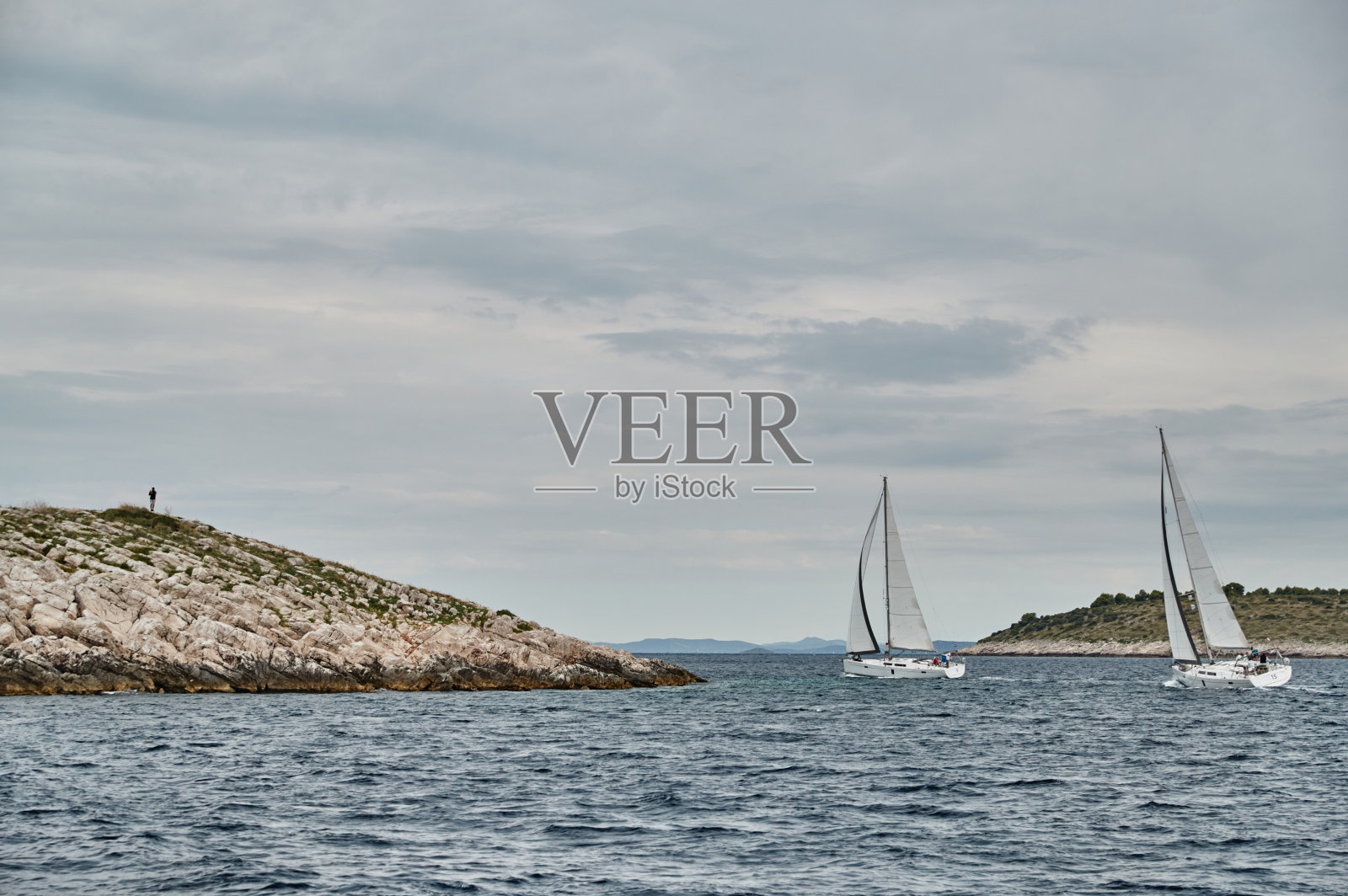 前景是帆船的海景，背景是岛上的男人，克罗地亚，一个多岩石的海岸照片摄影图片