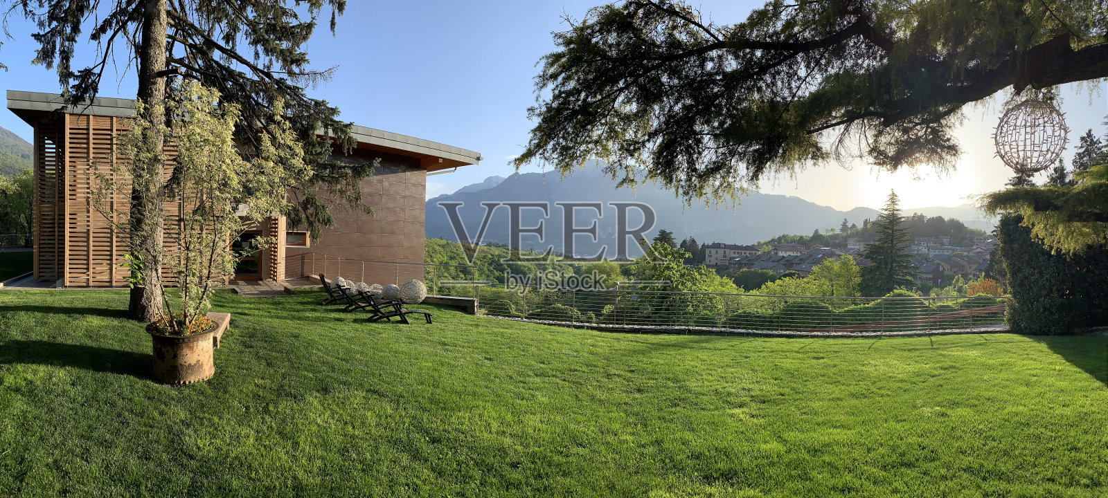 马德鲁佐别墅的领土全景在日落，巨大的树木，理想的绿色草坪，建筑的正面，风景如画的山透过傍晚的烟雾照片摄影图片