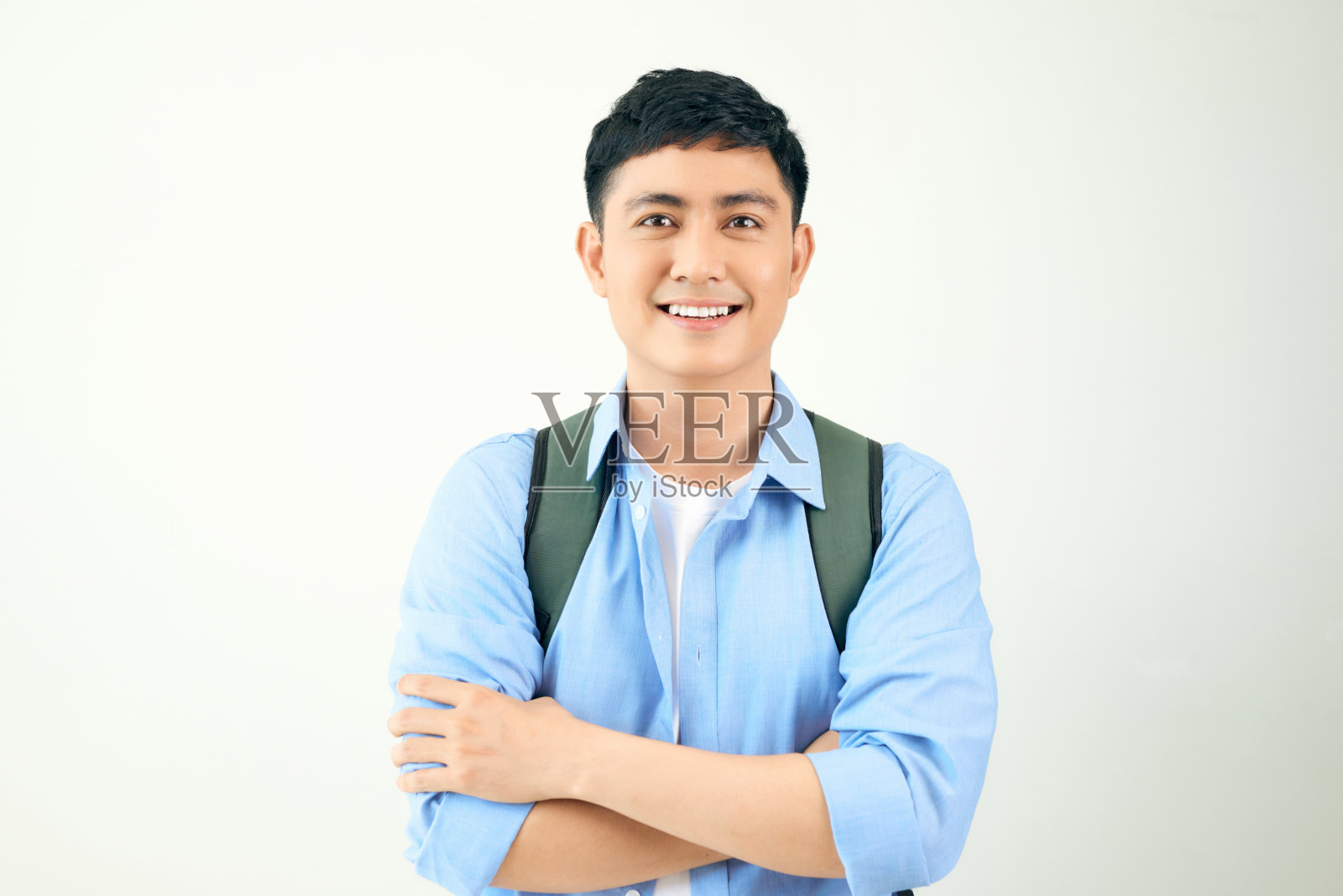 年轻男人在白色背景上交叉双臂，背着背包照片摄影图片