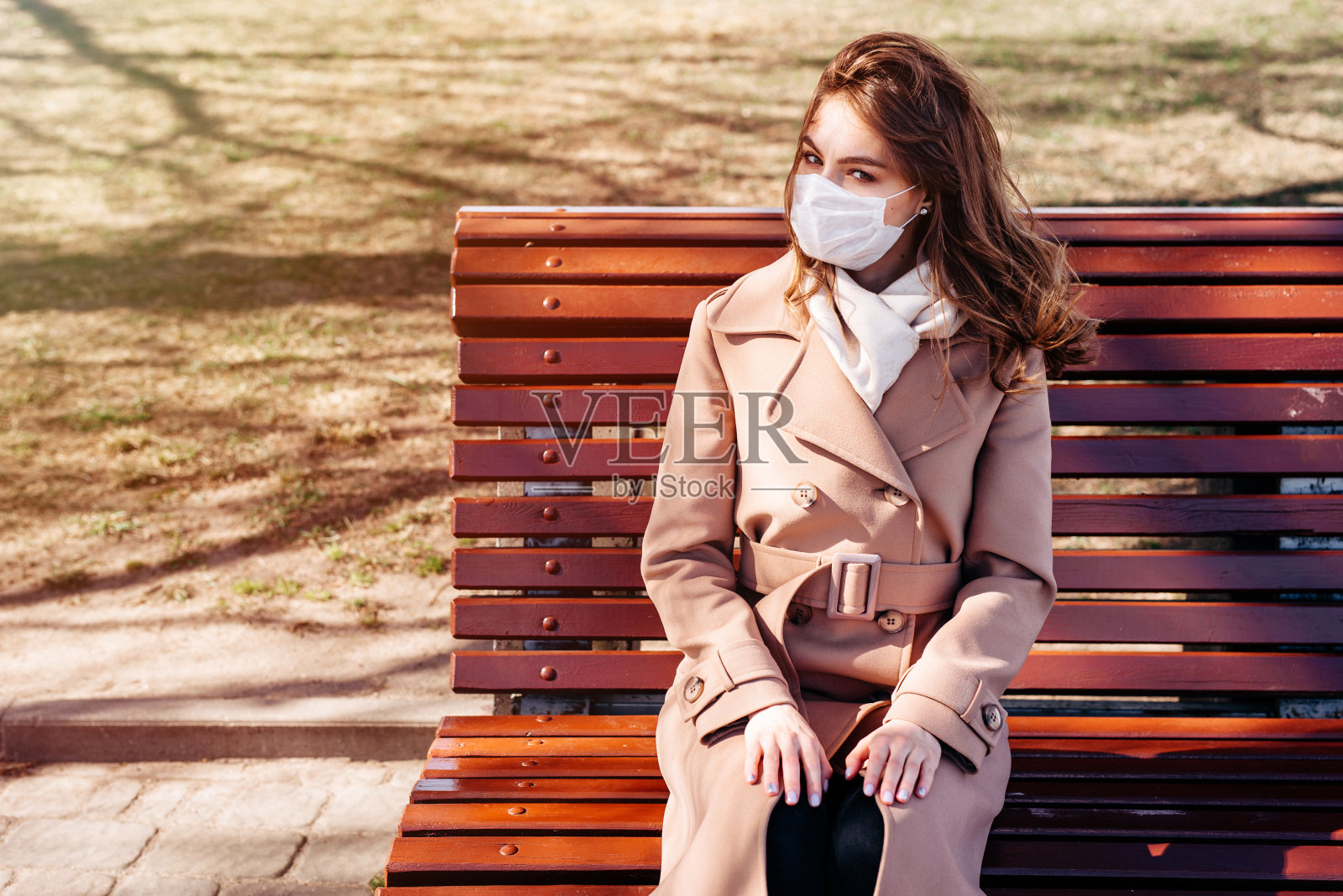 年轻漂亮的女人戴着防护医用口罩坐在公园的长椅上照片摄影图片