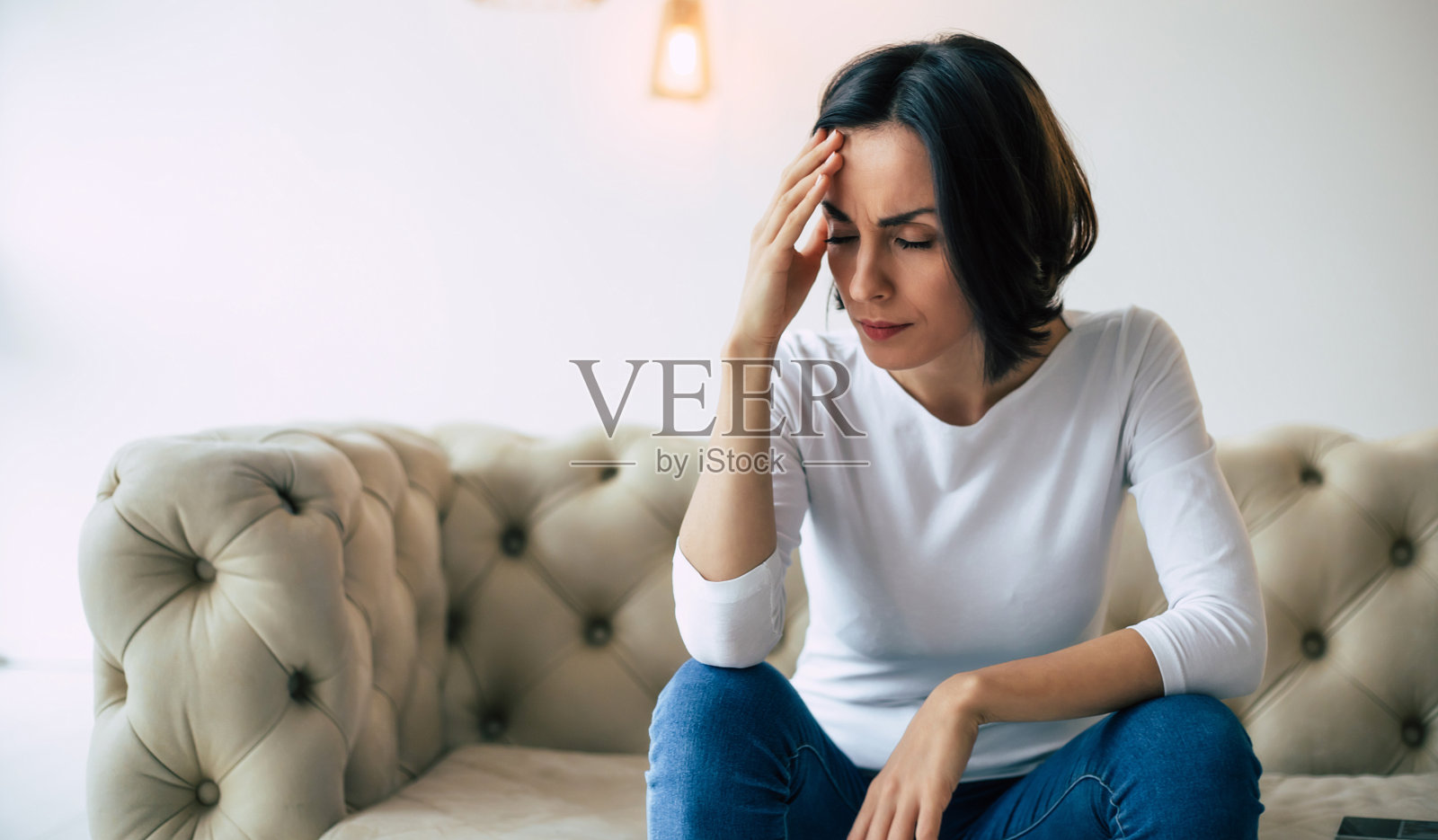 无法忍受头痛。深色头发的女人穿着休闲的衣服坐在她的沙发上，触摸她的头，同时呕吐和头痛。照片摄影图片