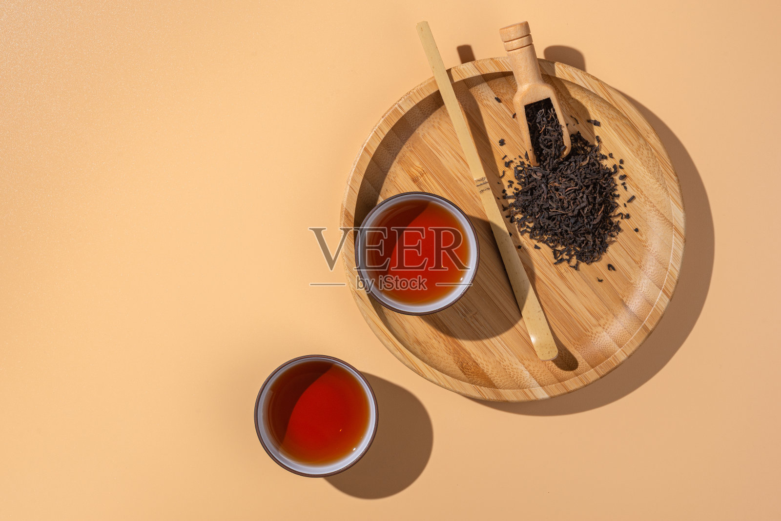 两个装有黑茶的陶瓷碗，在米色的背景上用竹木盘子和勺子盛着干普洱茶。照片摄影图片