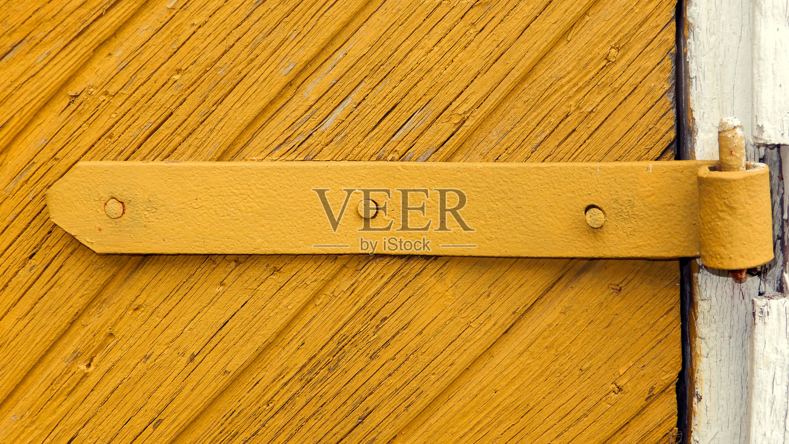 金属门铰链装在旧的黄色木门上。照片摄影图片