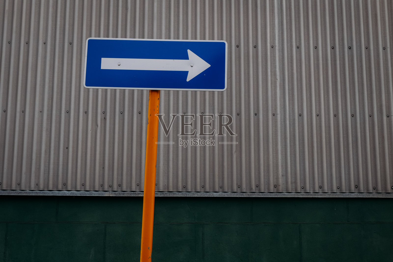 黄色柱子上的蓝色标志与灰色的金属墙相衬，表明了向右的方向照片摄影图片