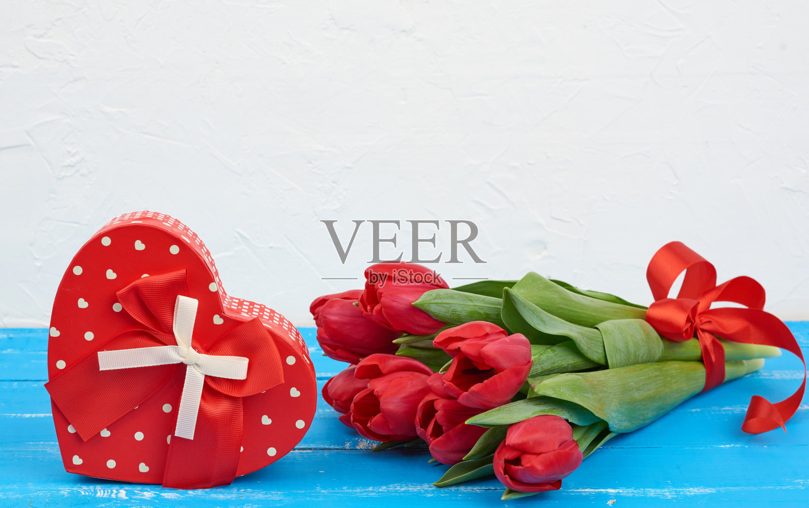 一束红色盛开的郁金香和绿色的叶子，包装礼物在蓝色的木制背景照片摄影图片